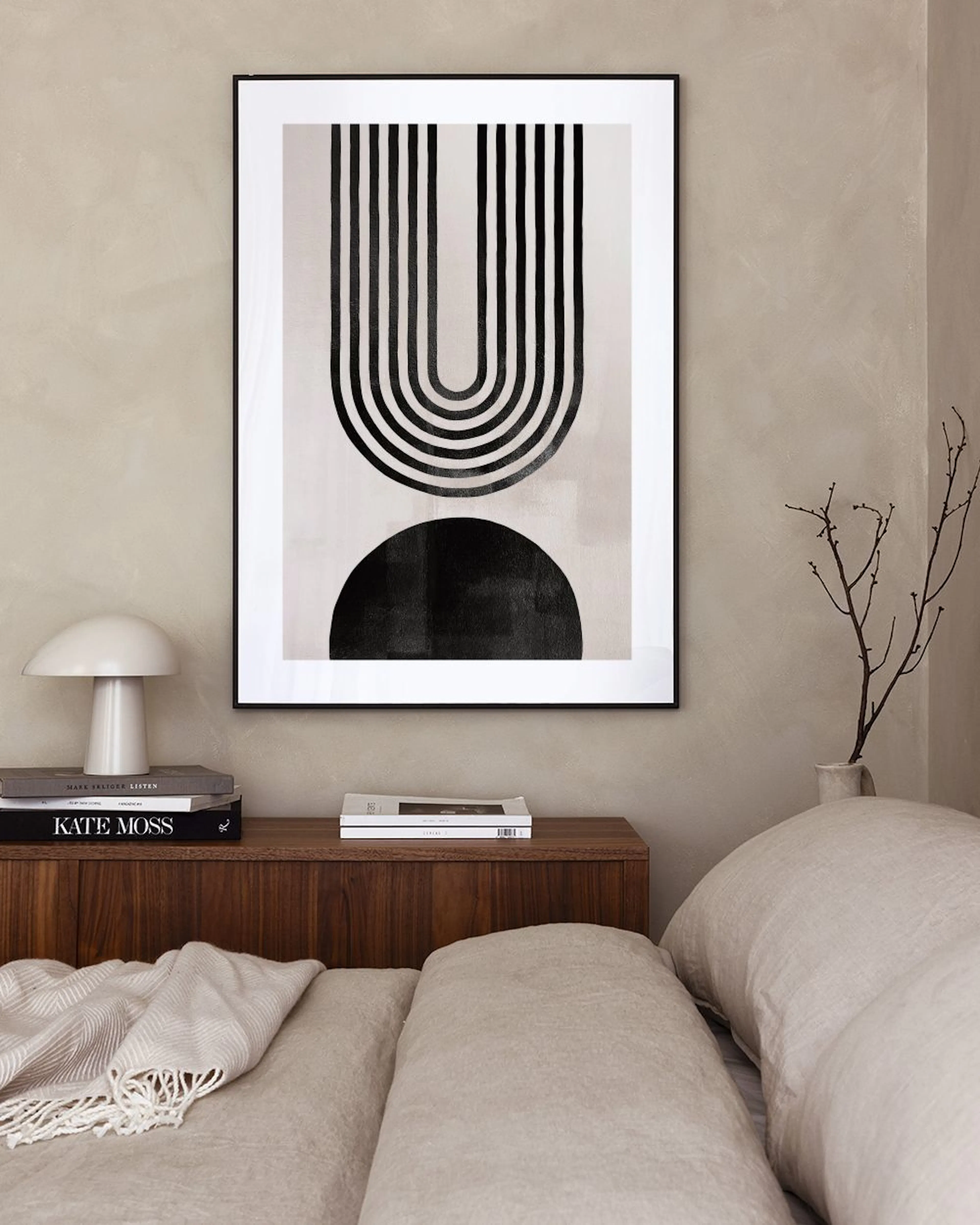 Plakat med abstrakt mønster av svarte, buede linjer og halvsirkel, henger over en hvit kommode med lampe og vase.