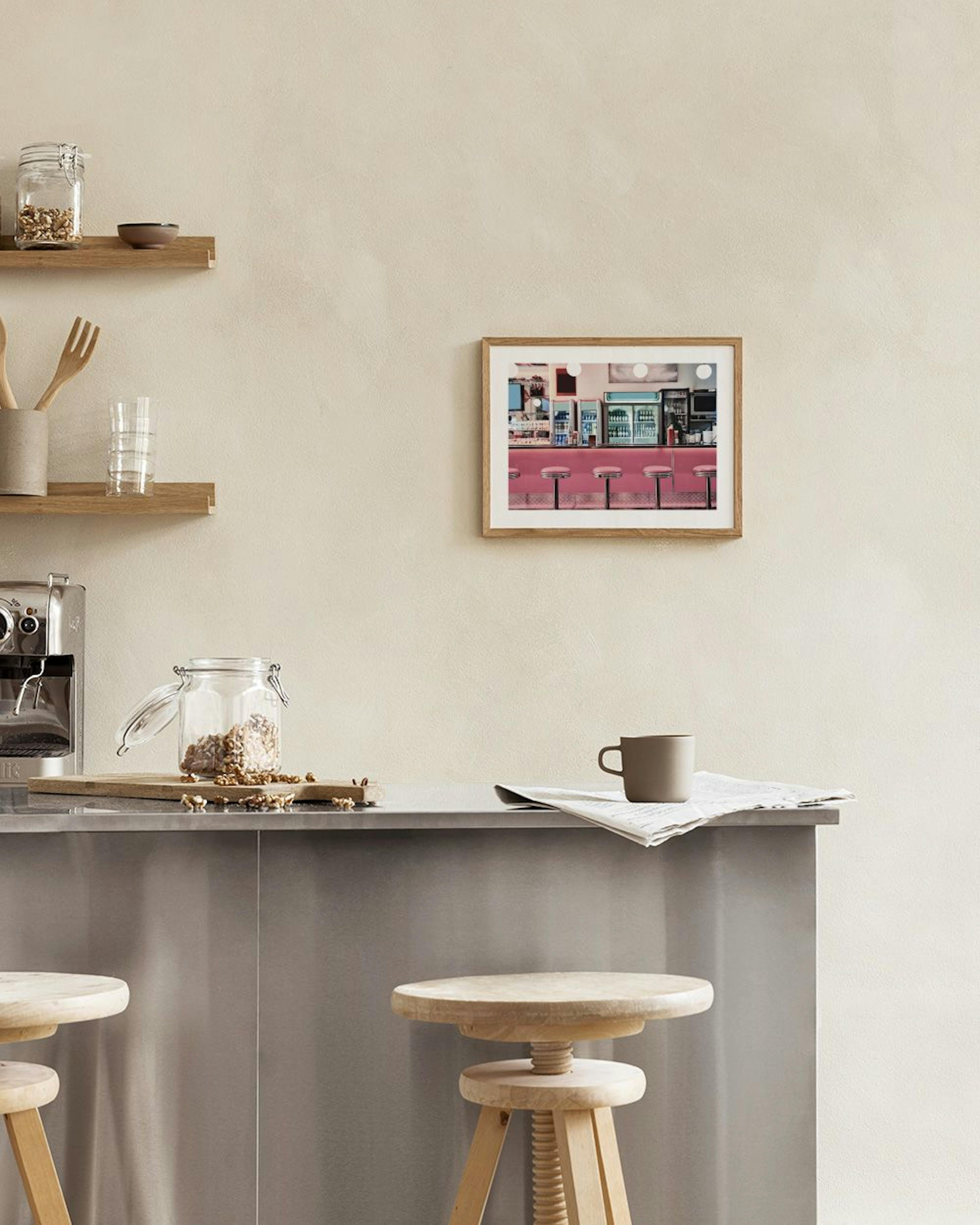 Póster de um balcão de café americano com bancos rosa, exibido numa bancada com um vaso e livros.
