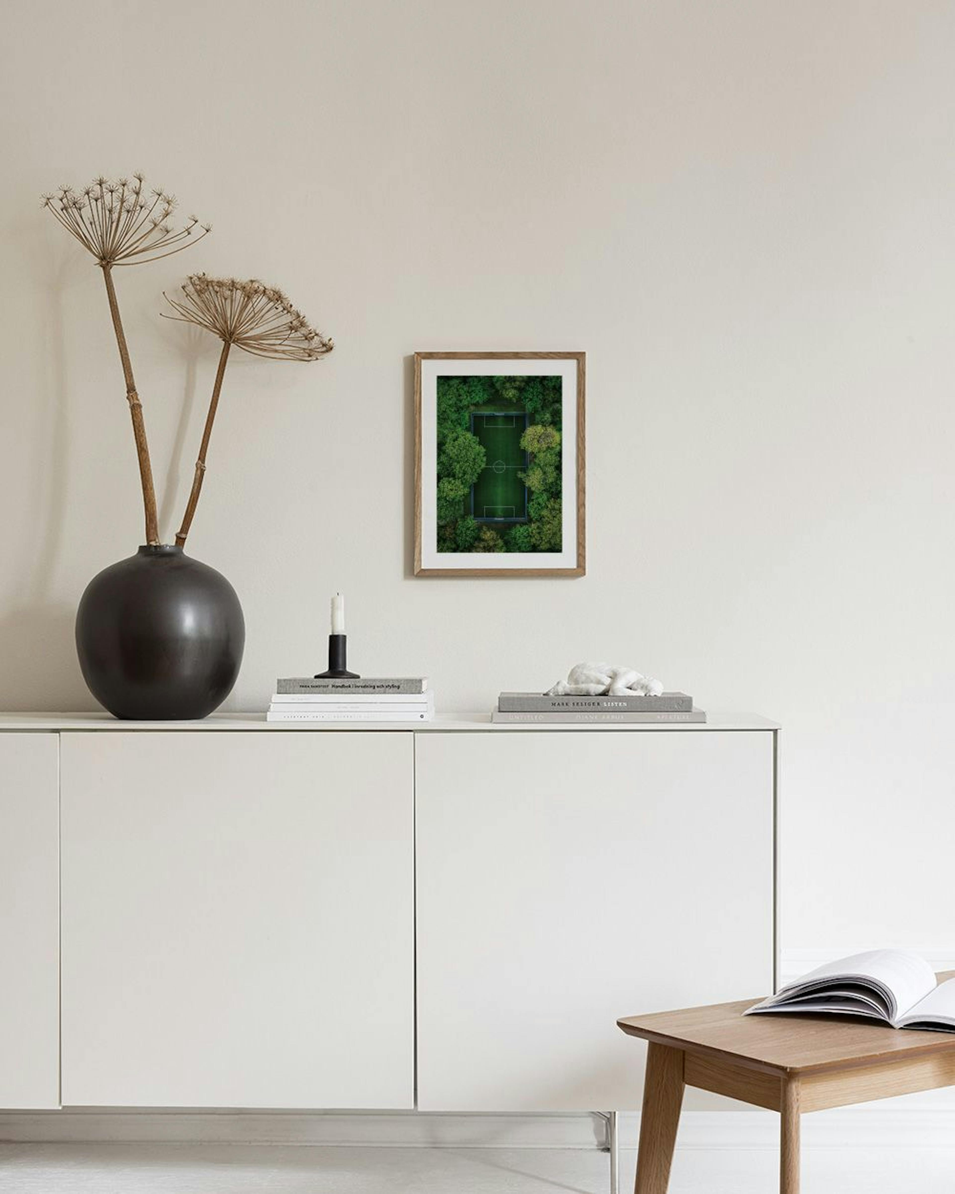 Poster van een voetbalveld omringd door bomen, hangend boven een poef in een moderne kamer.