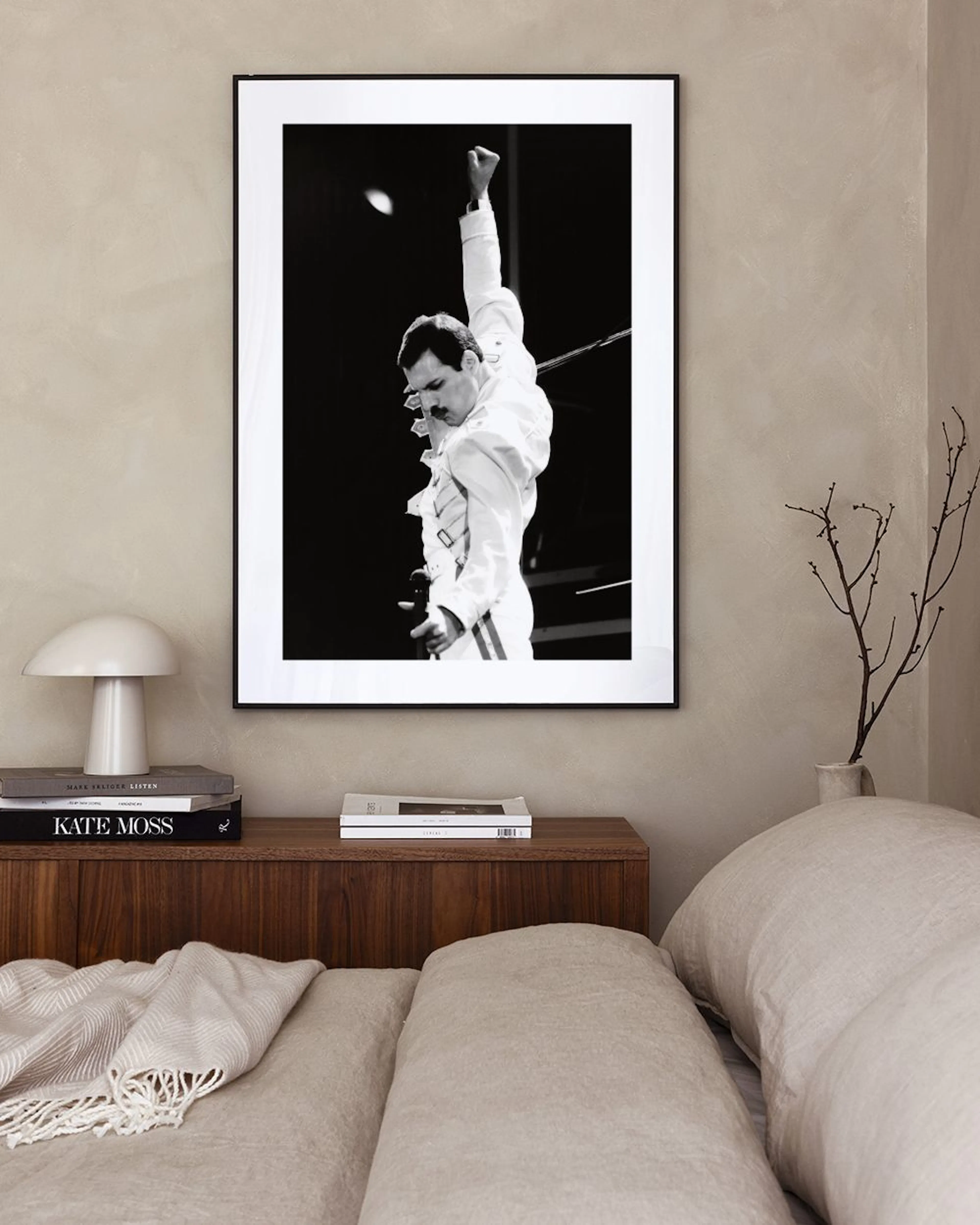 Póster en blanco y negro de Freddie Mercury con el puño en alto, colgado sobre un puf en una sala moderna.