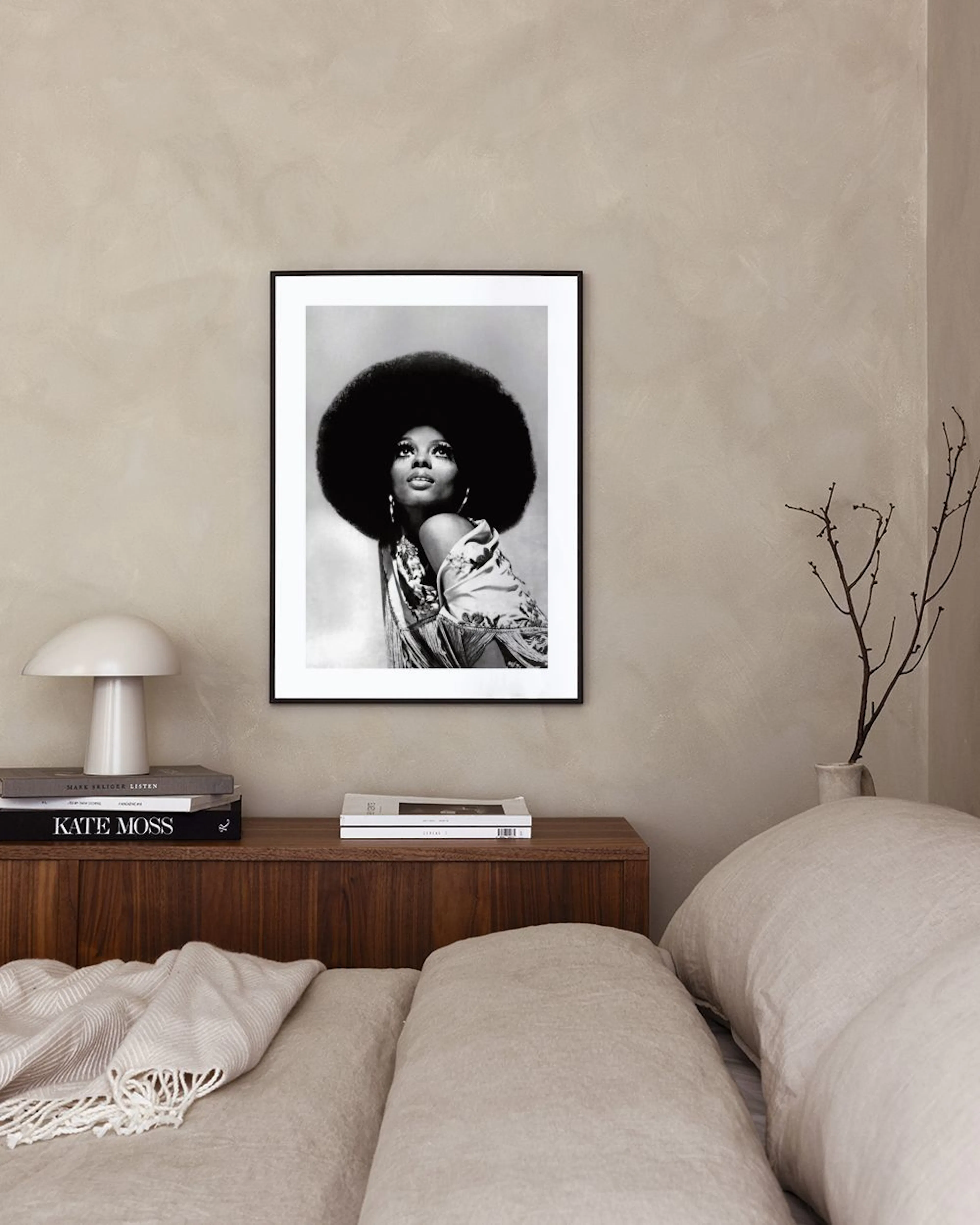 A black and white print of a woman with a large afro, looking up, hanging on a gray wall next to pampas grass and a beige armcha