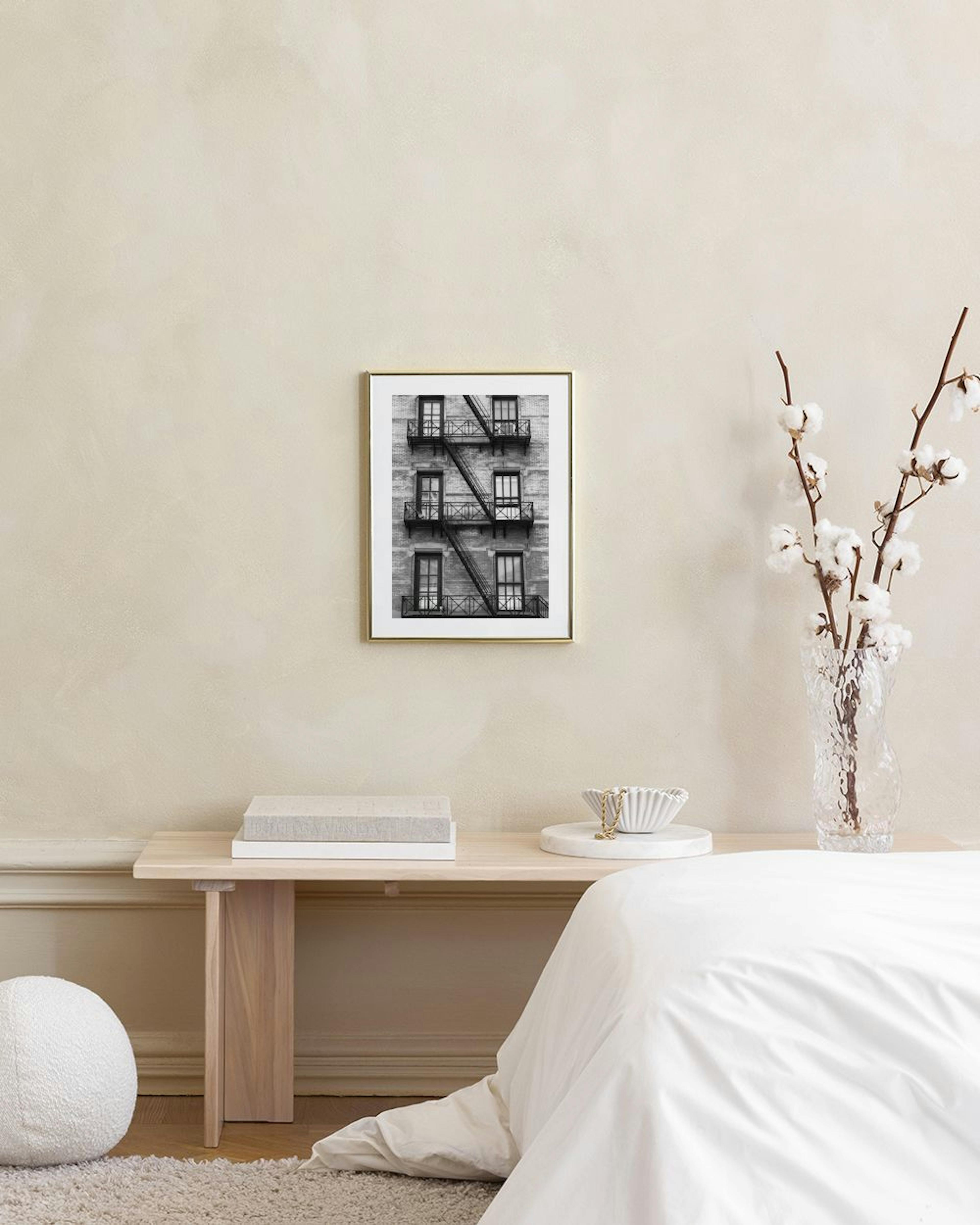Black and white print of a brick building with fire escapes, hanging above a marble table with vases and books.