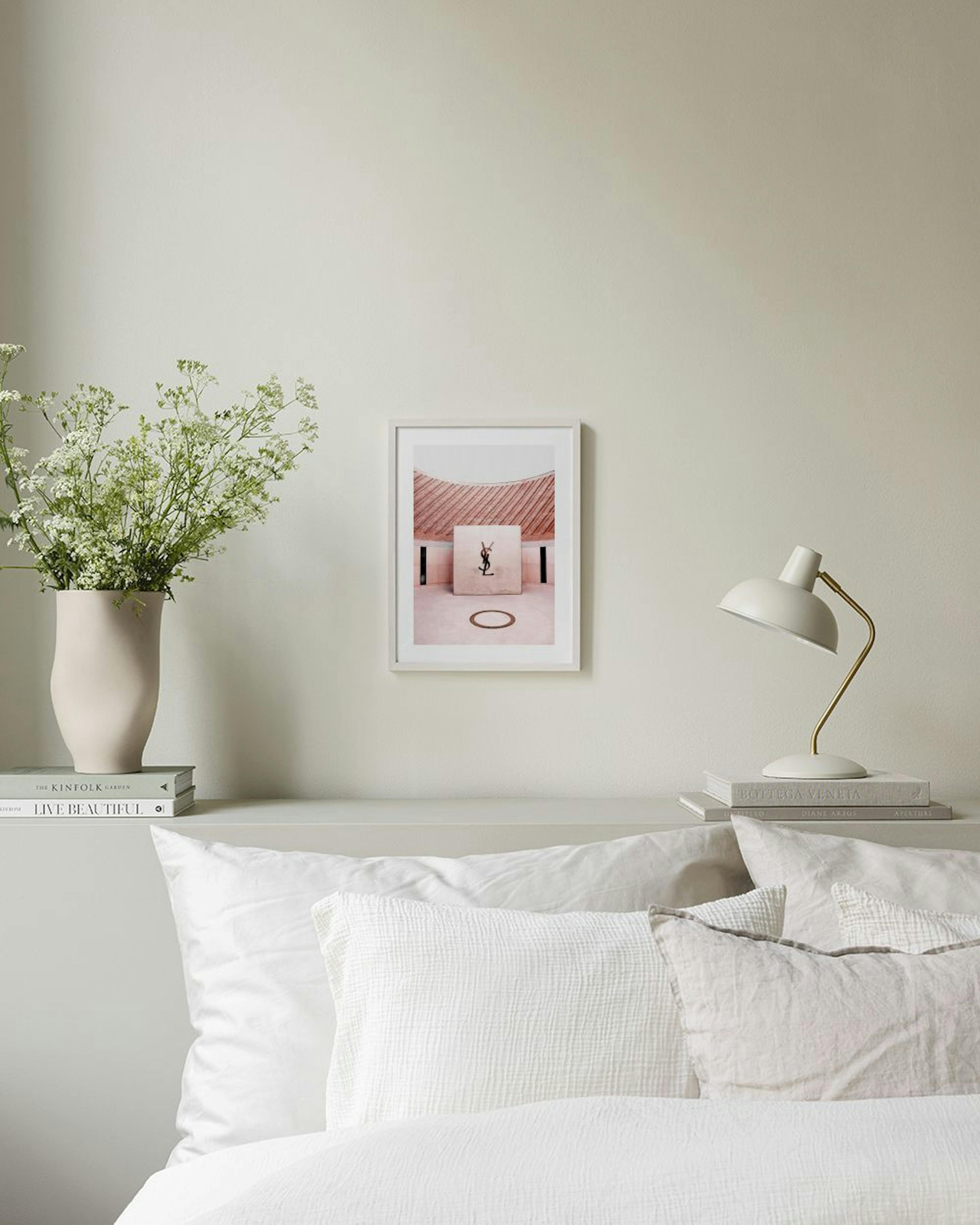 Póster de una caja Yves Saint Laurent rosa en un entorno arquitectónico, colgado sobre un mueble con libros y decoración.