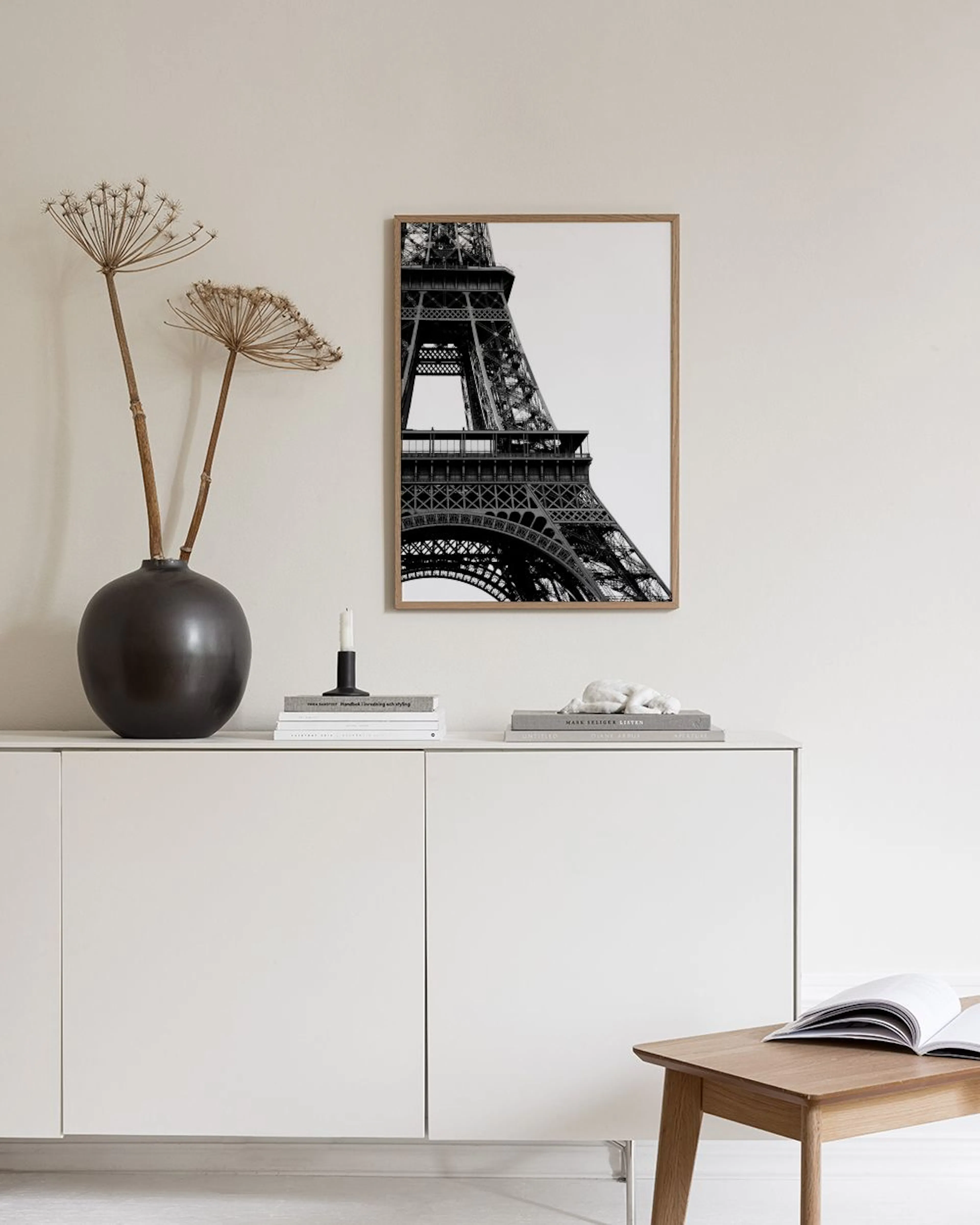 A black and white print of the Eiffel Tower, displayed above a dark timber buffet with a white textured bowl and books.