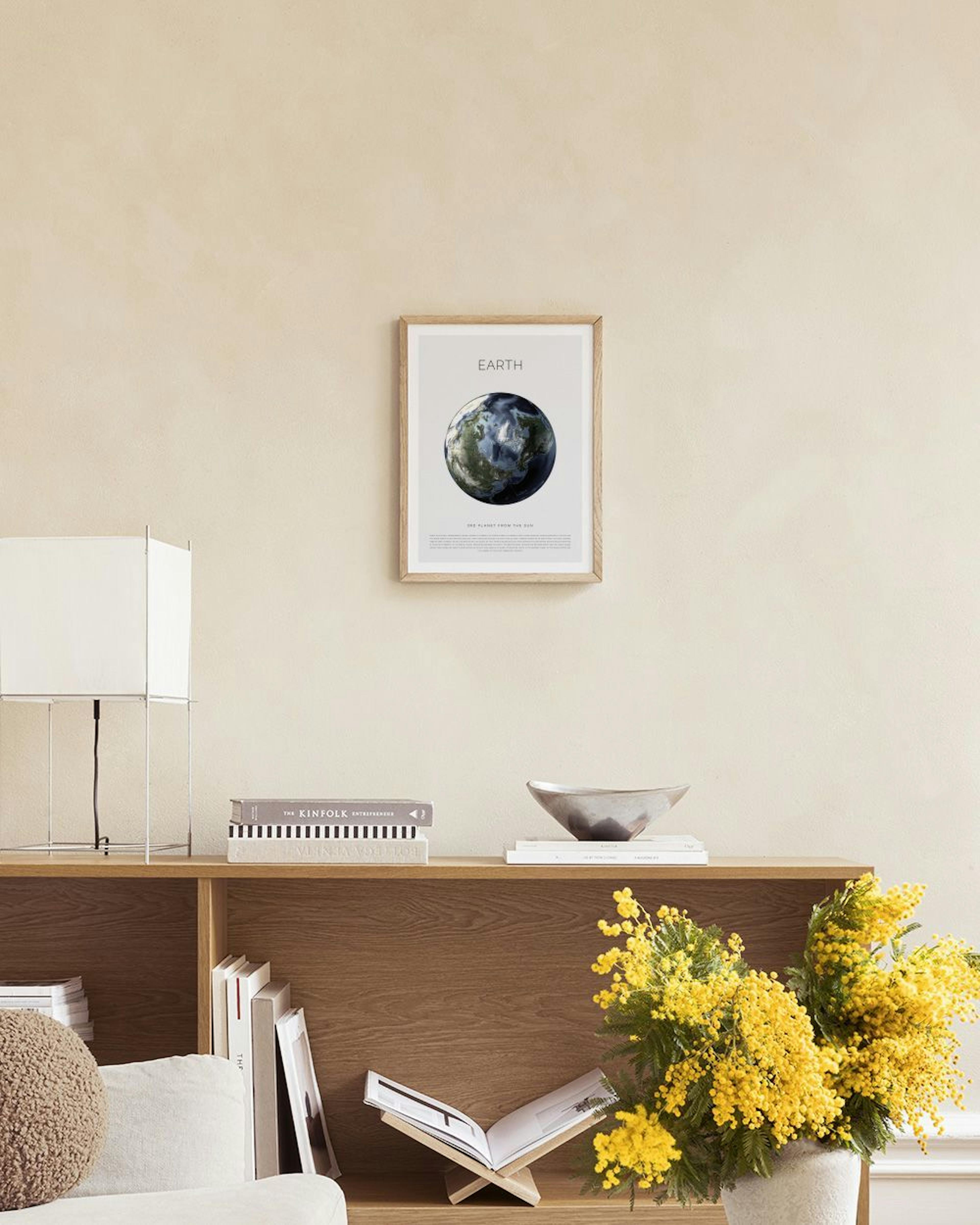 Poster della Terra con paesaggi verdi e oceani blu, appeso sopra una panca in rattan con libri, in un ambiente minimalista.