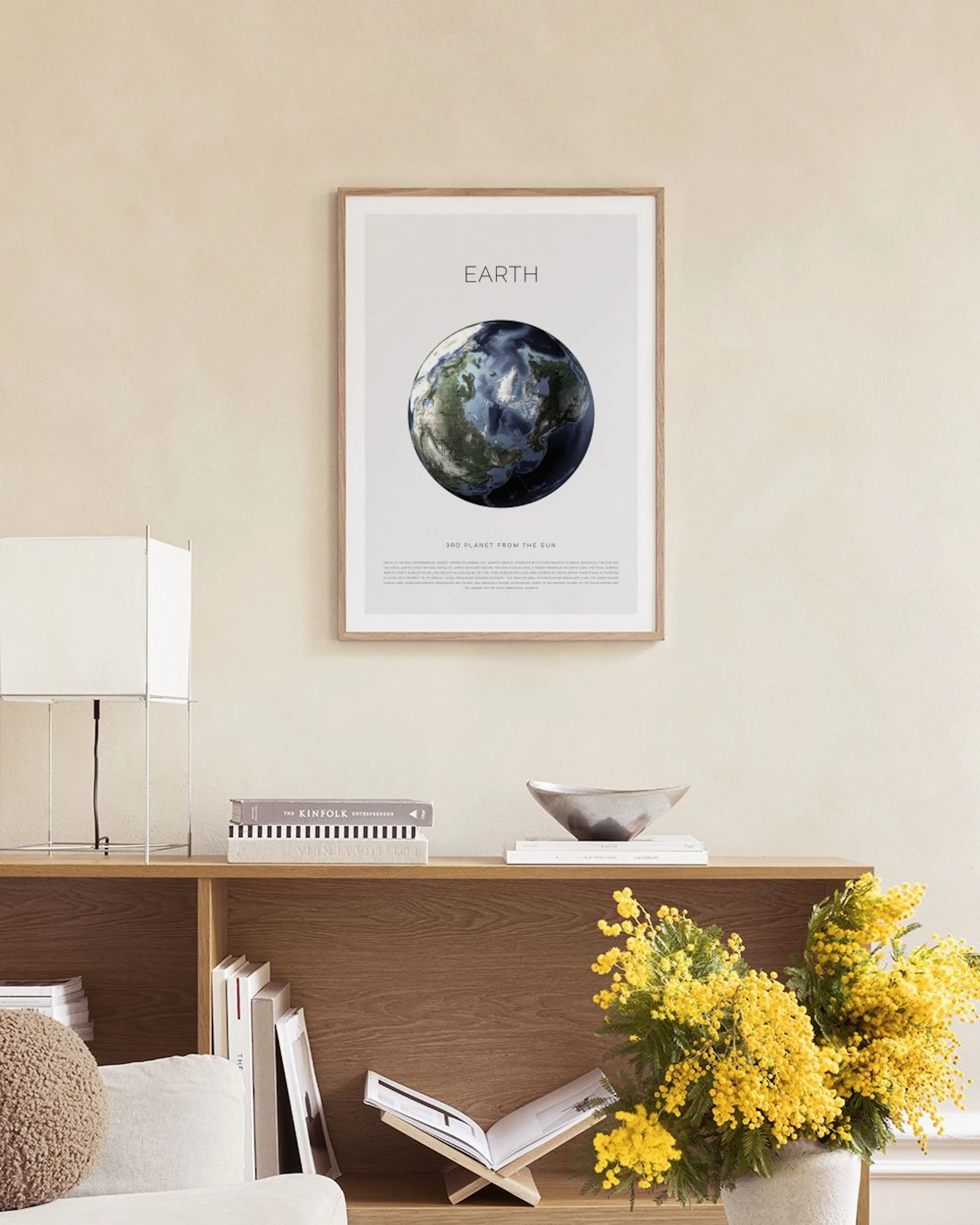 An Earth globe print hangs above a woven wooden bench with books in a modern room.