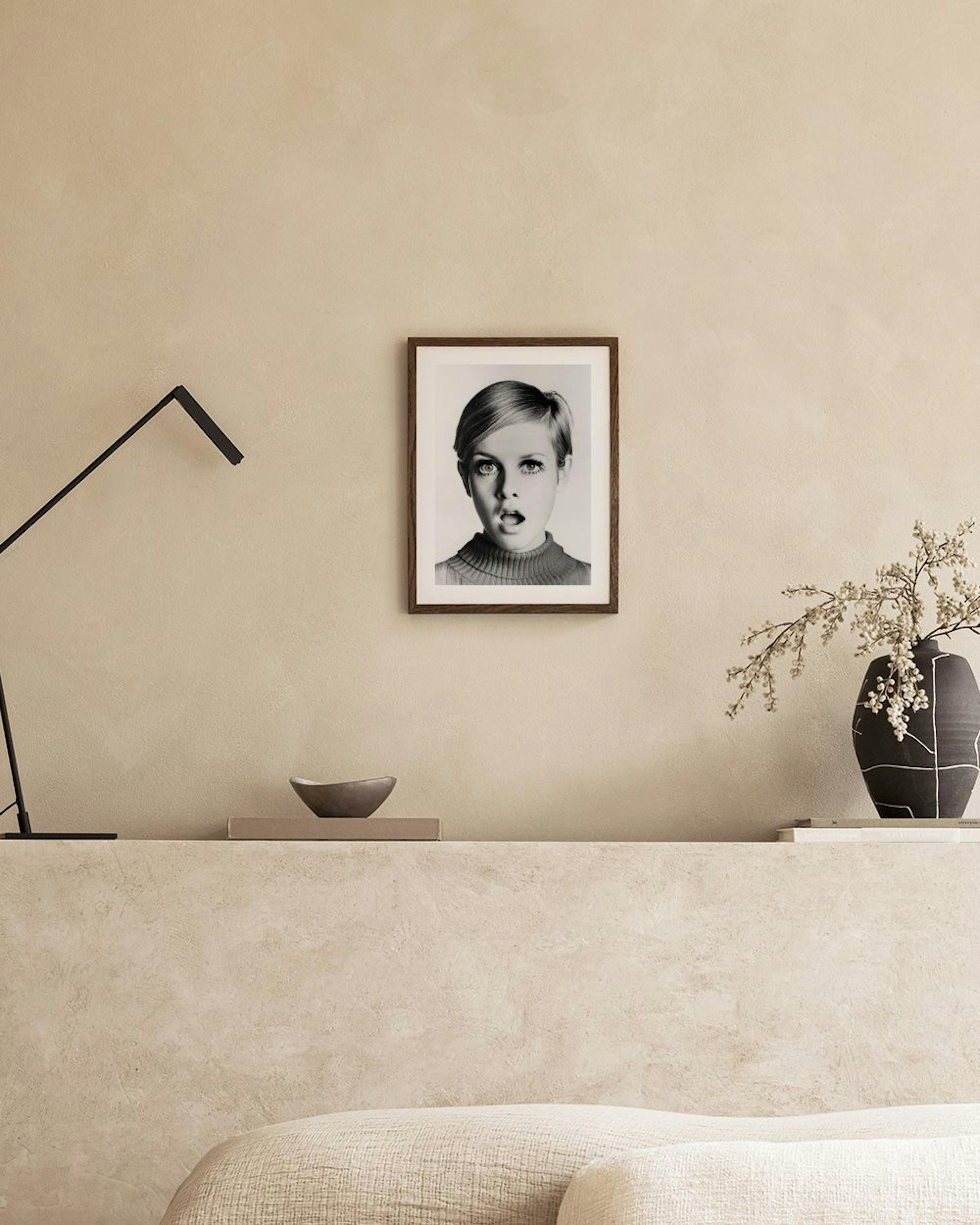 Affiche Twiggy en noir et blanc, accrochée au-dessus dune table en béton avec un plateau et un vase.