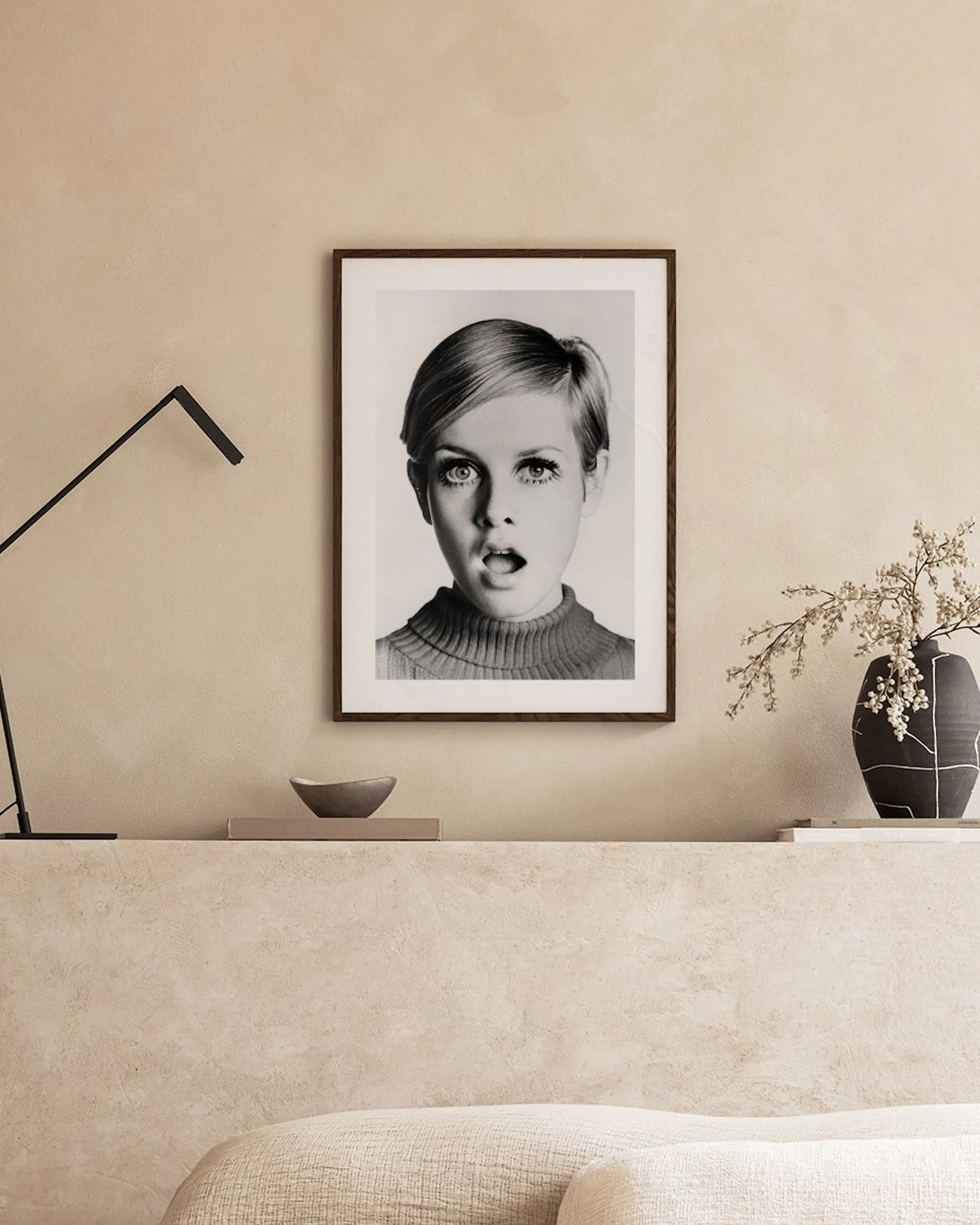 Póster en blanco y negro de Twiggy con la boca abierta, colgado sobre un banco de piedra con jarrones y un cuenco.