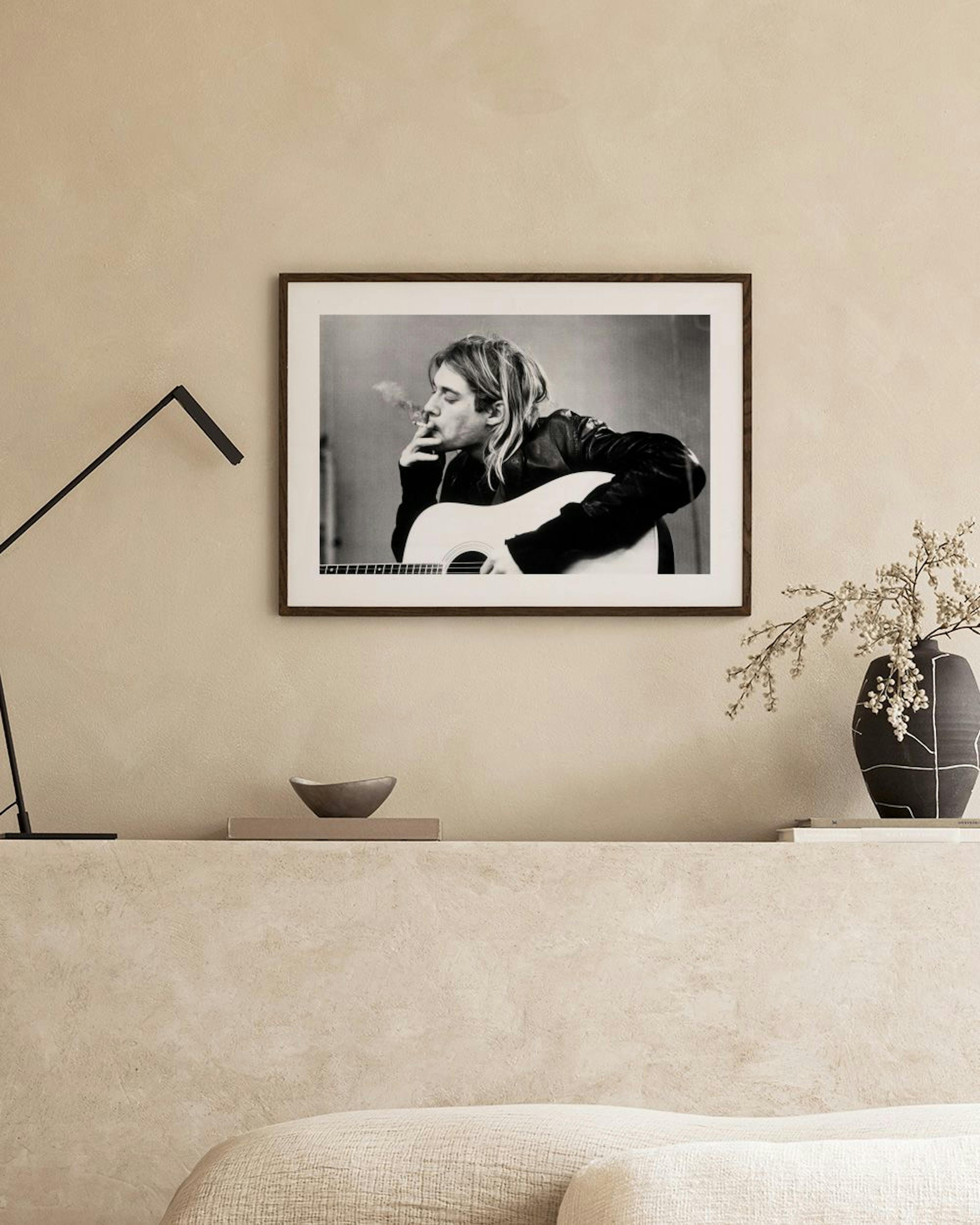 Black and white print of Kurt Cobain with a guitar and cigarette, hanging above a concrete bench in a modern room.
