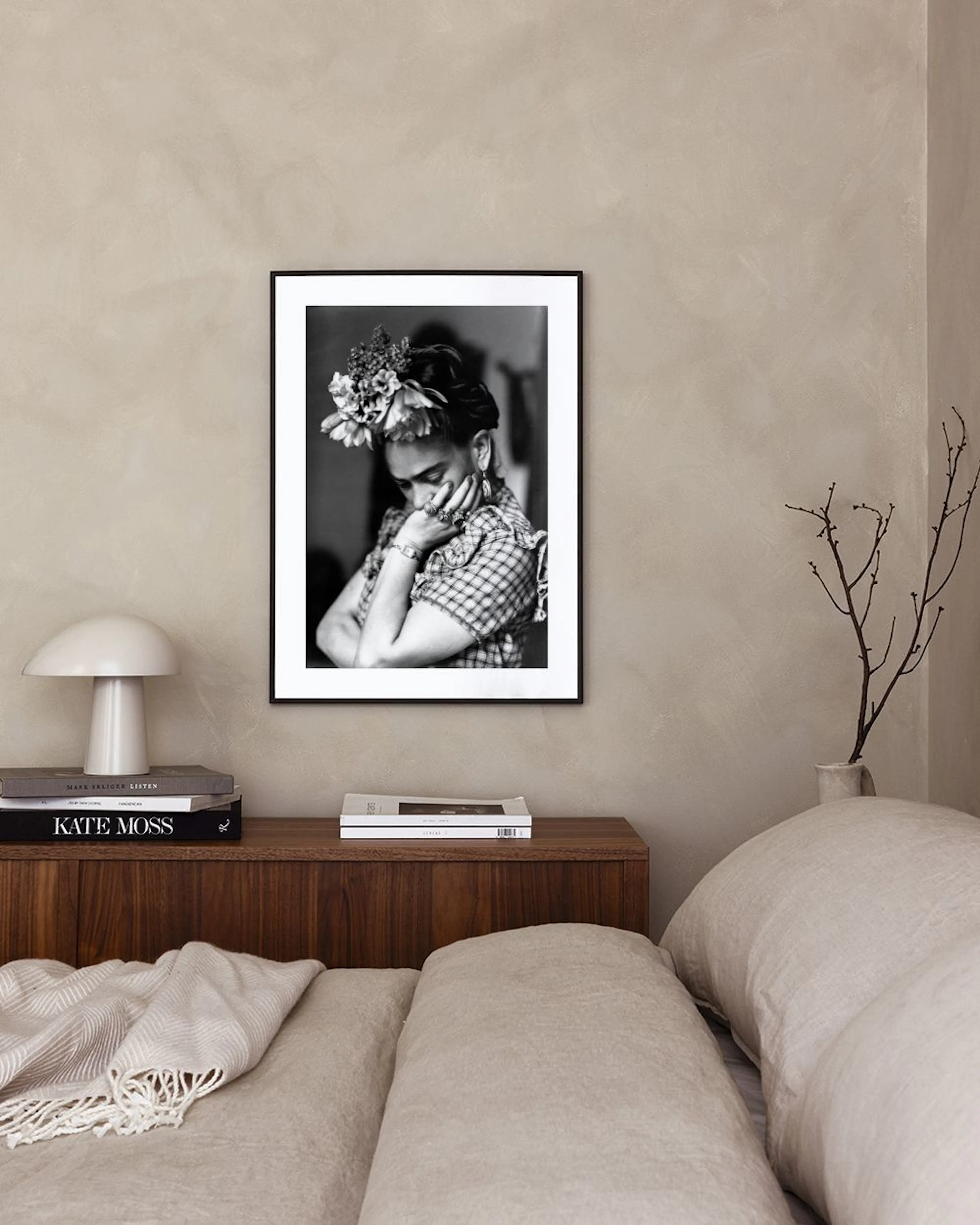 Póster de Frida Kahlo en blanco y negro, con flores en el cabello, exhibido sobre una cómoda blanca en una sala moderna.