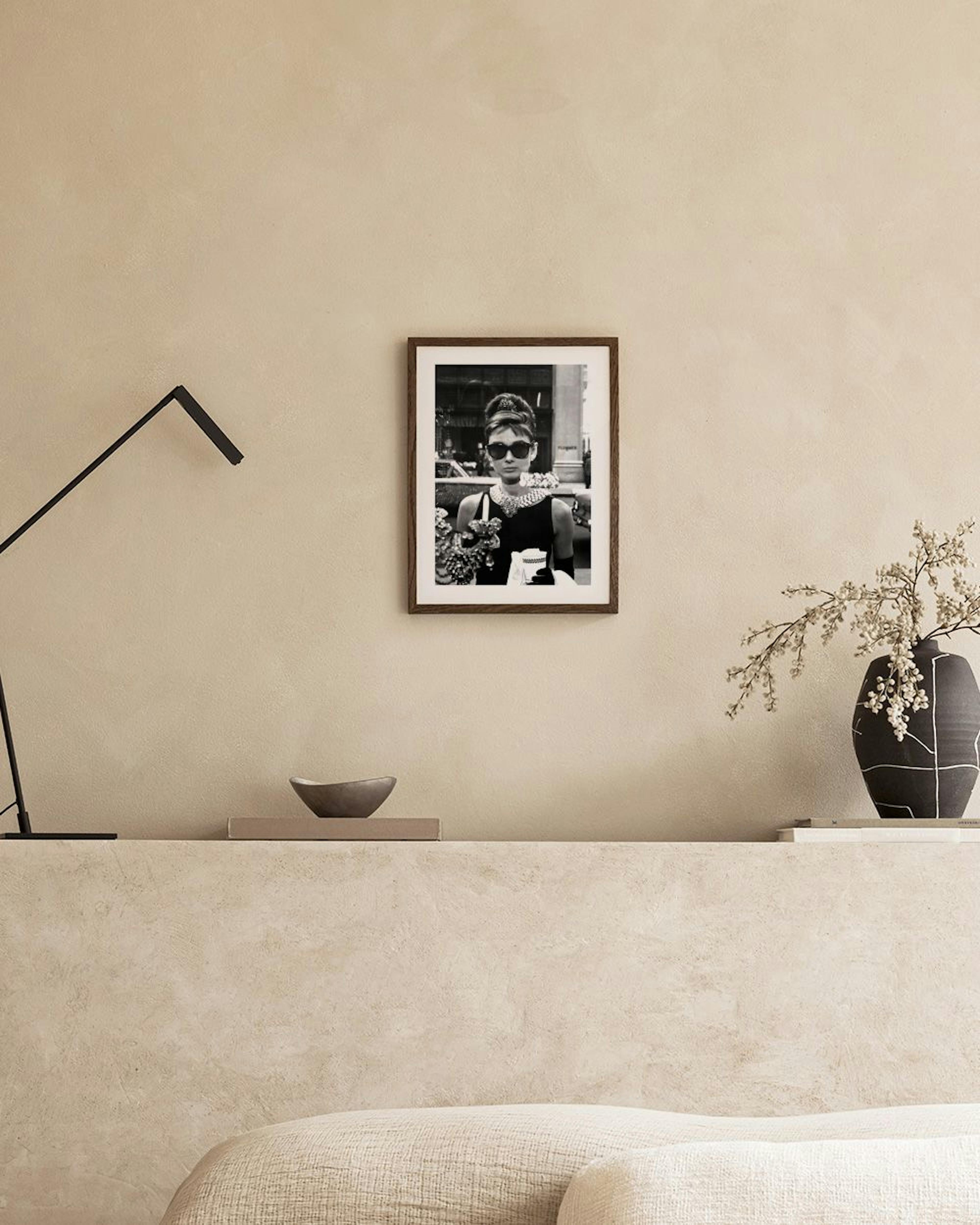 Póster en blanco y negro de Audrey Hepburn con gafas de sol, expuesto sobre una mesa de cemento con jarrones en una sala moderna