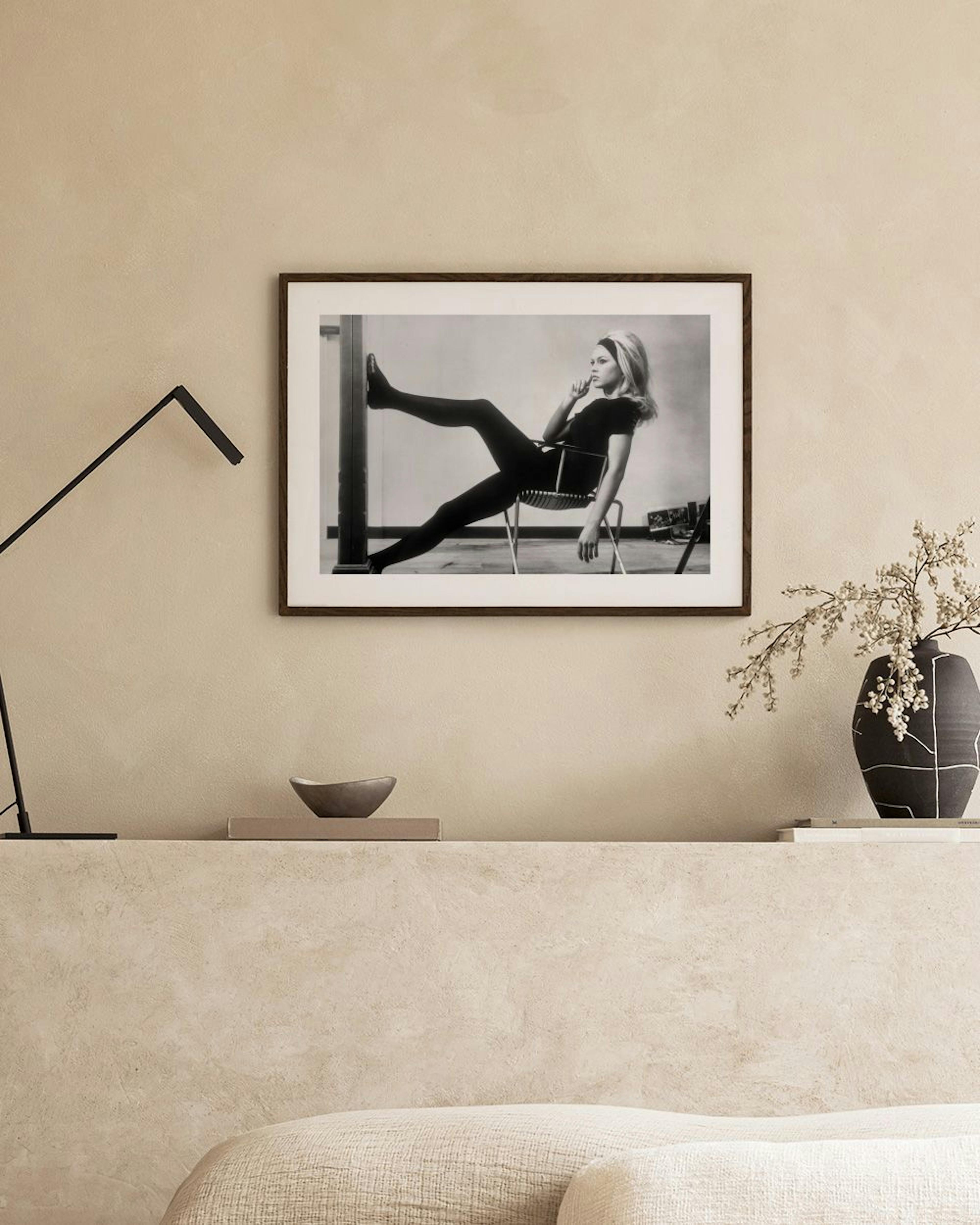Black and white print of Brigitte Bardot in a chair, displayed above a console table with a vase and books.