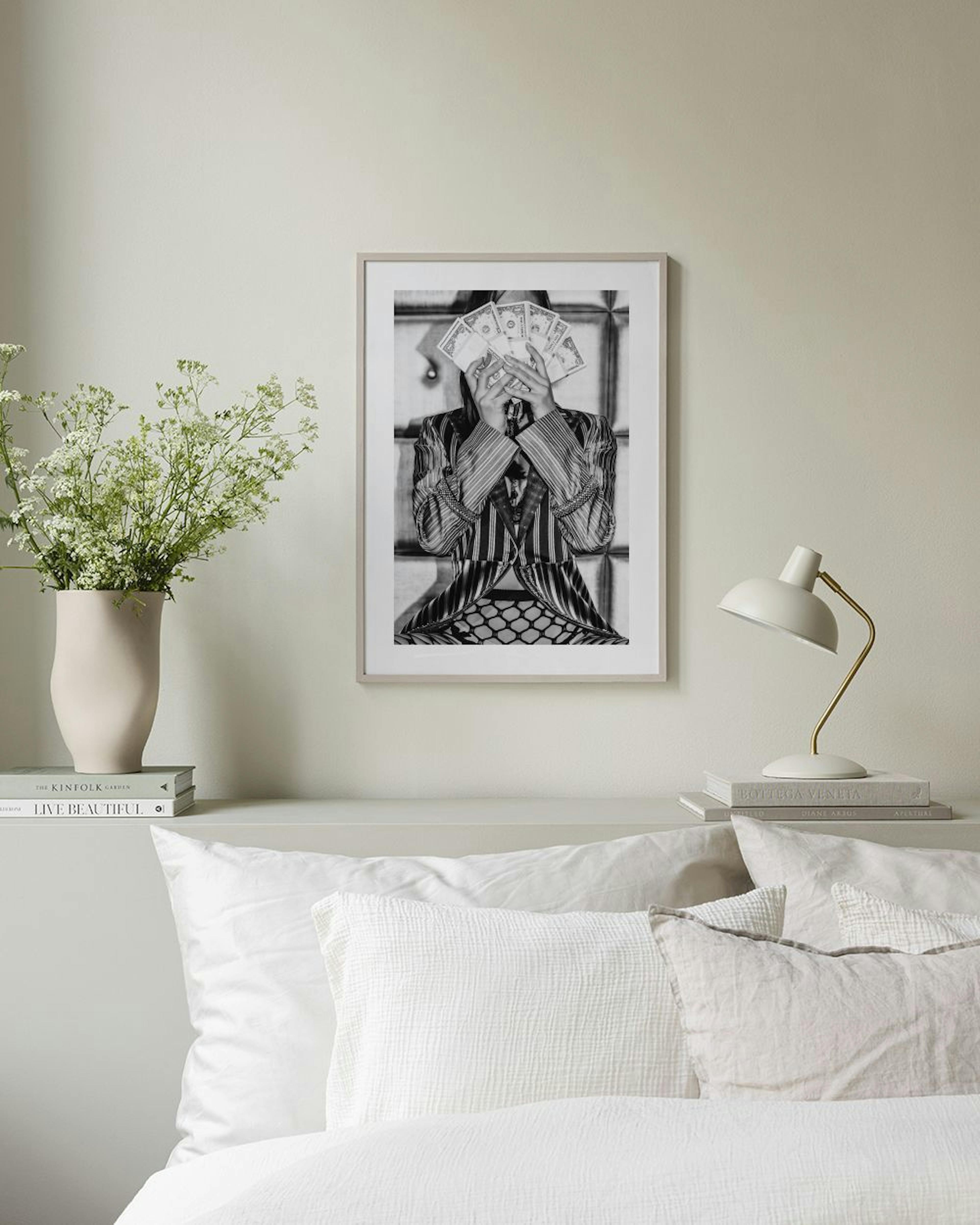 Poster in bianco e nero di una persona che tiene banconote davanti al viso, appeso sopra un mobile bianco con un vaso rotondo.