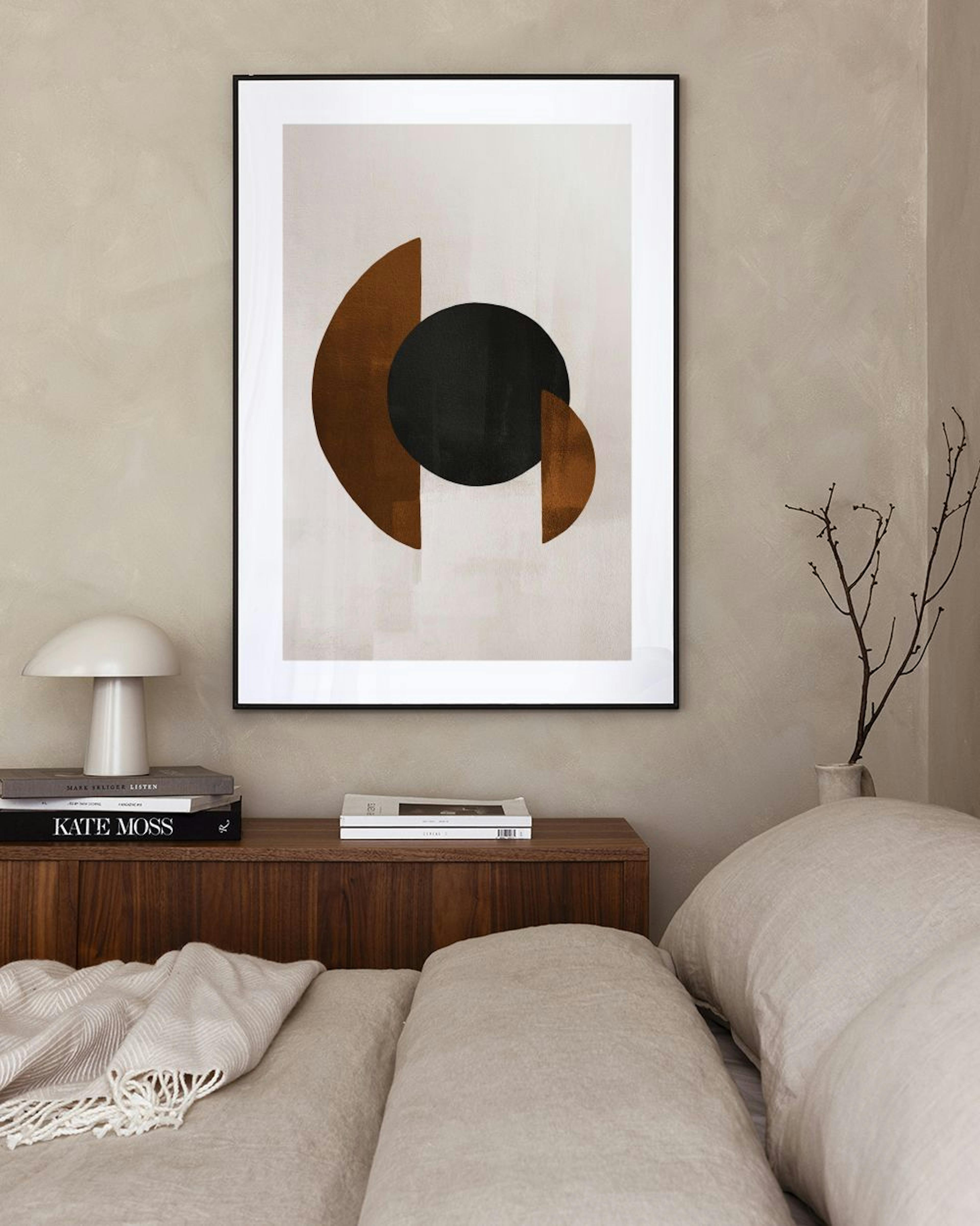 A print of a black circle and two brown half-circles on a light background, hanging above a gray chair and next to a tall cactus