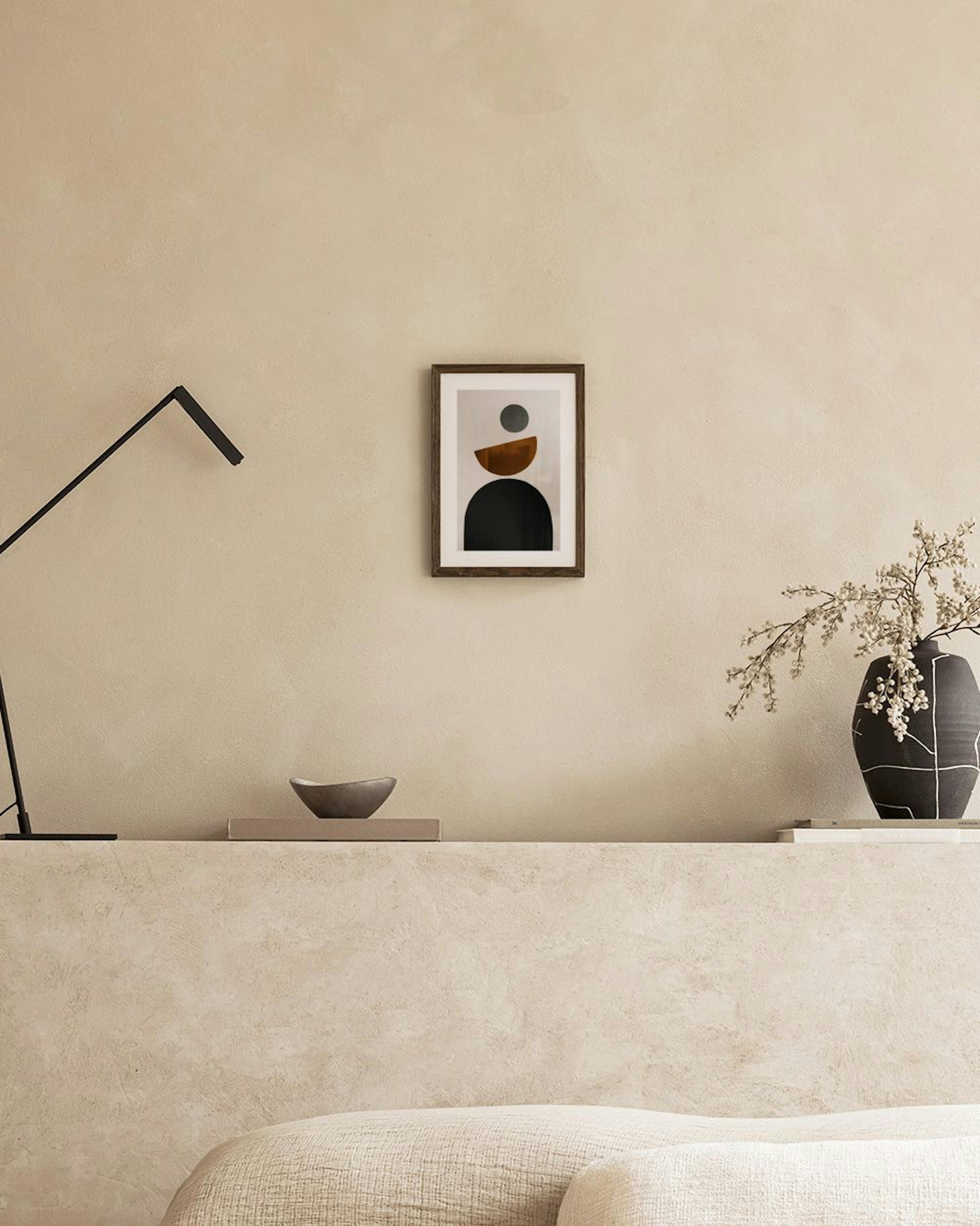 Abstract print with black, brown, and grey geometric shapes, displayed in a minimal living room above a brown ottoman.