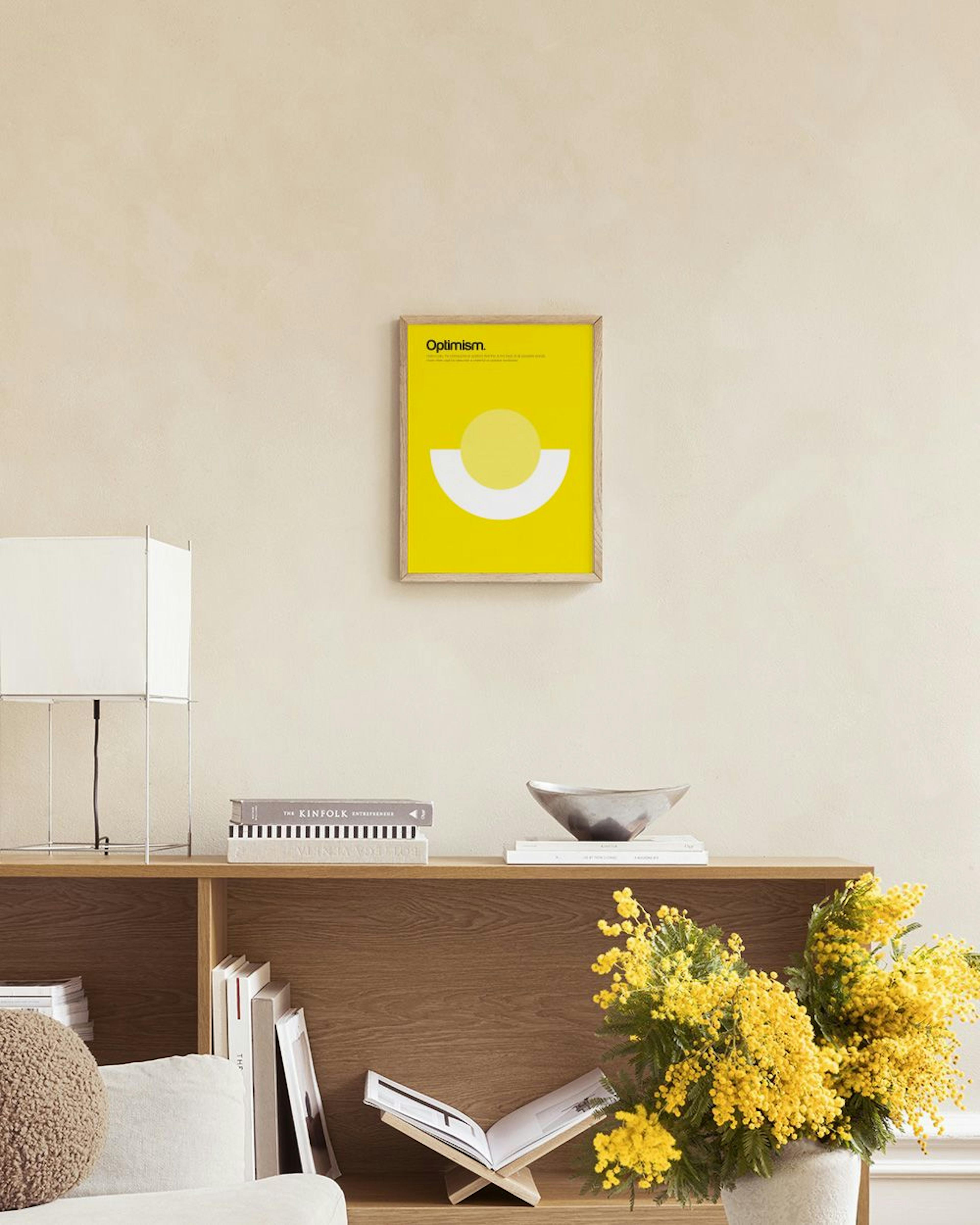 Gelbes Poster Optimism mit hellem Kreis und weißem Halbkreis, hängt über einer Rattanbank mit Büchern.