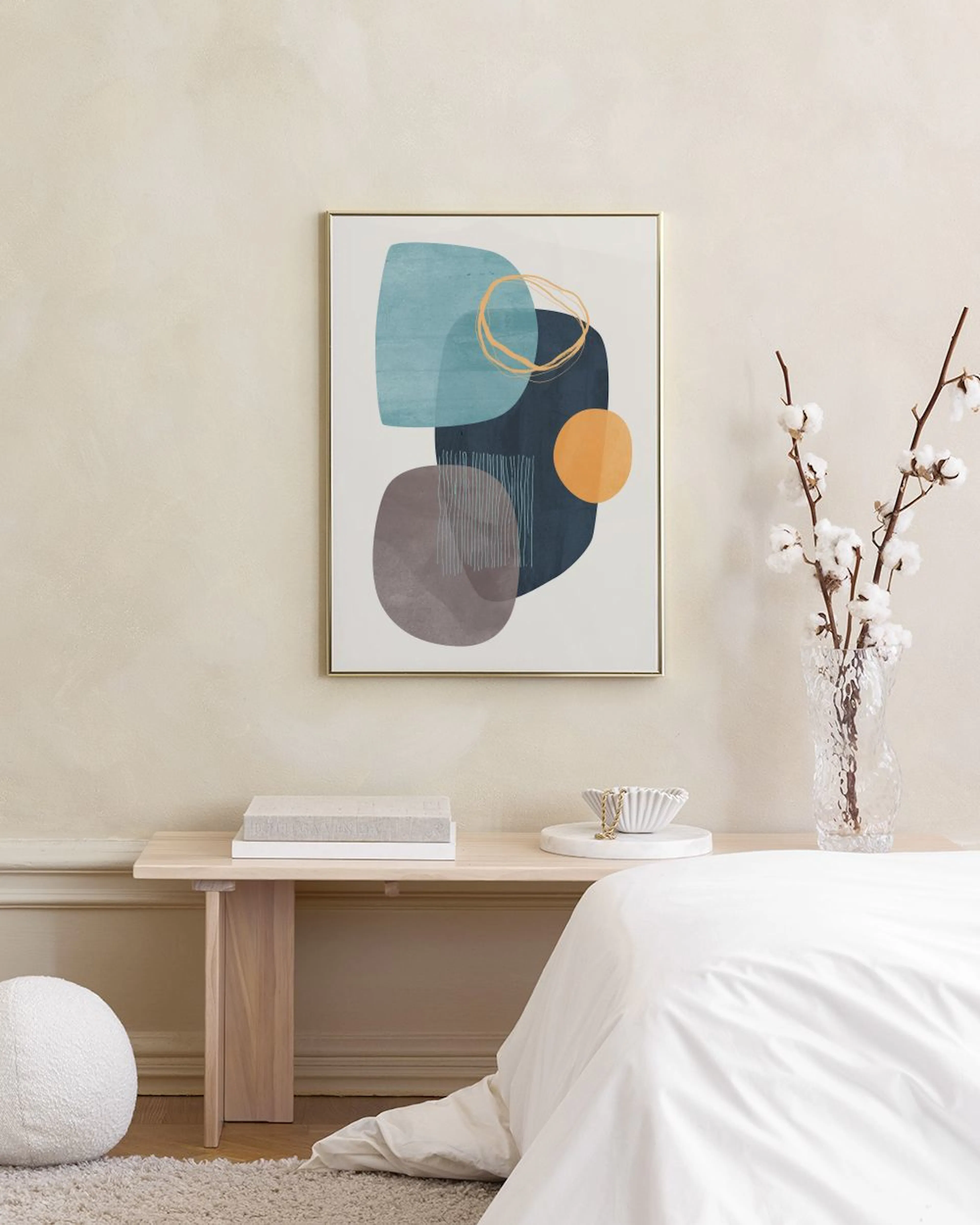 Poster astratto con forme organiche blu, grigie e arancioni, appeso sopra una credenza bianca con un vaso e libri.