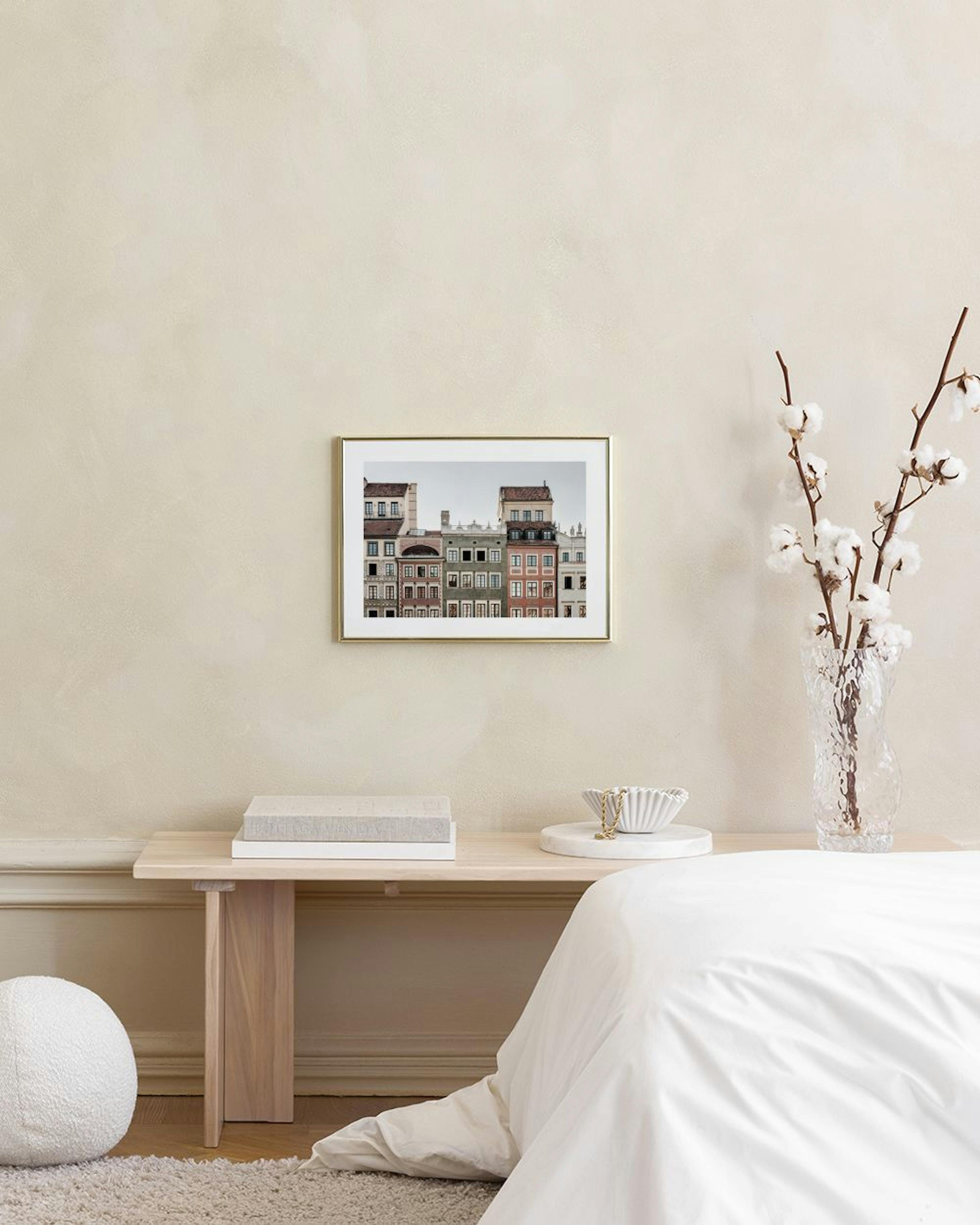 Poster con facciate di edifici colorati e finestre, appeso sopra un tavolino e una poltrona in un soggiorno moderno.