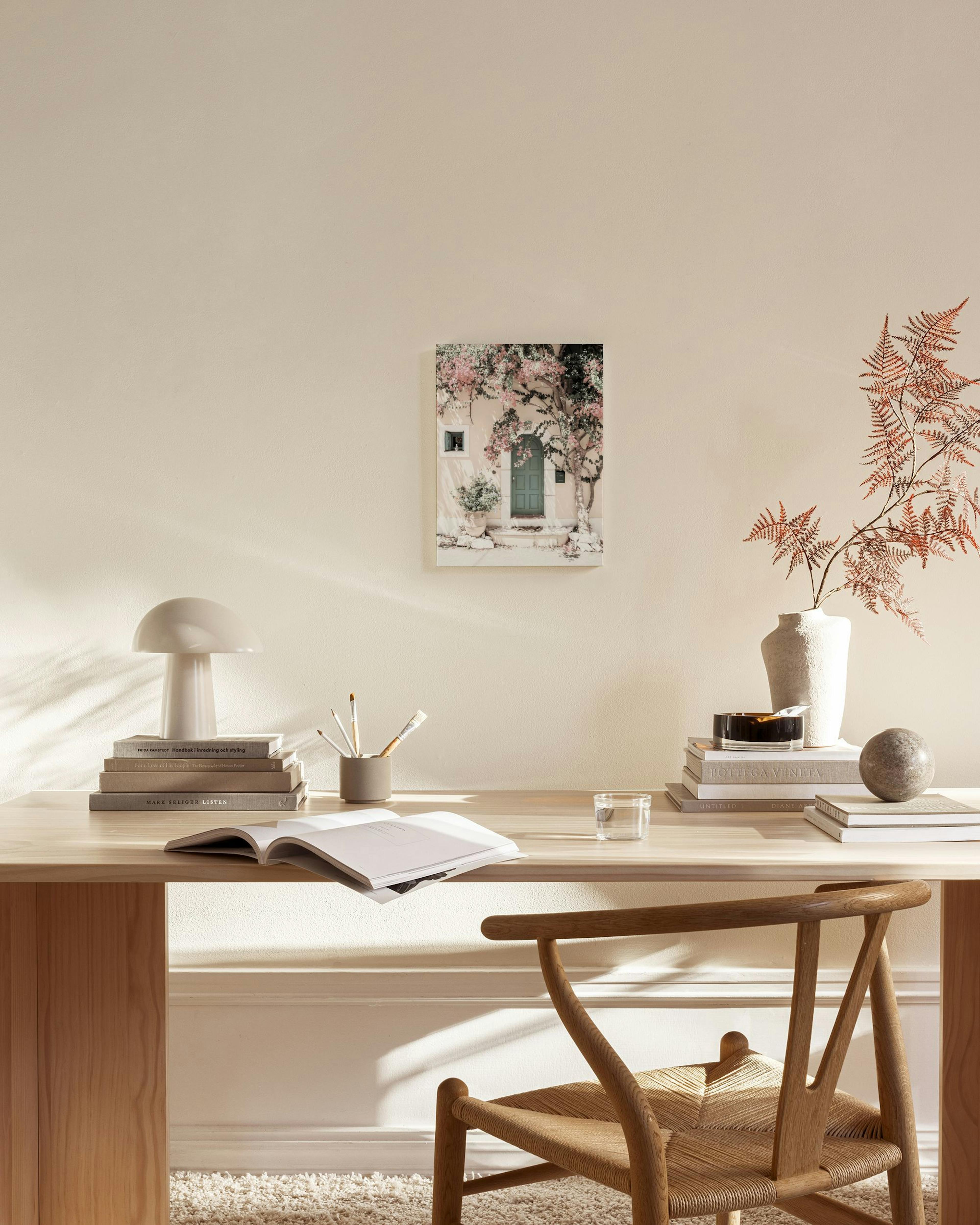 Canvas van een mintgroene deur omgeven door roze bloesem, hangend in een lichte woonkamer boven een houten dressoir.