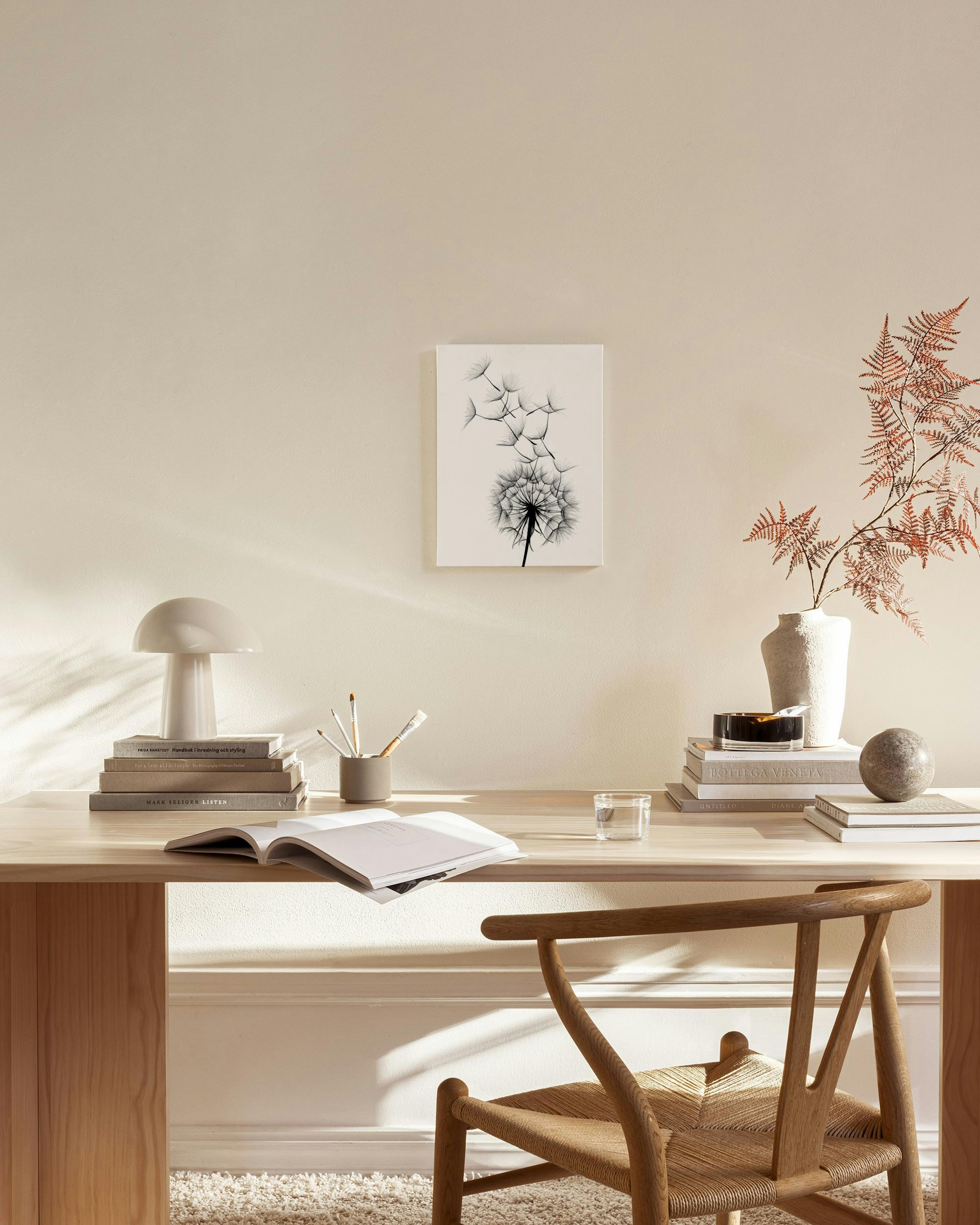 Tela decorativa com dente-de-leão preto e sementes a voar, pendurada numa sala de estar minimalista com móveis de madeira claros