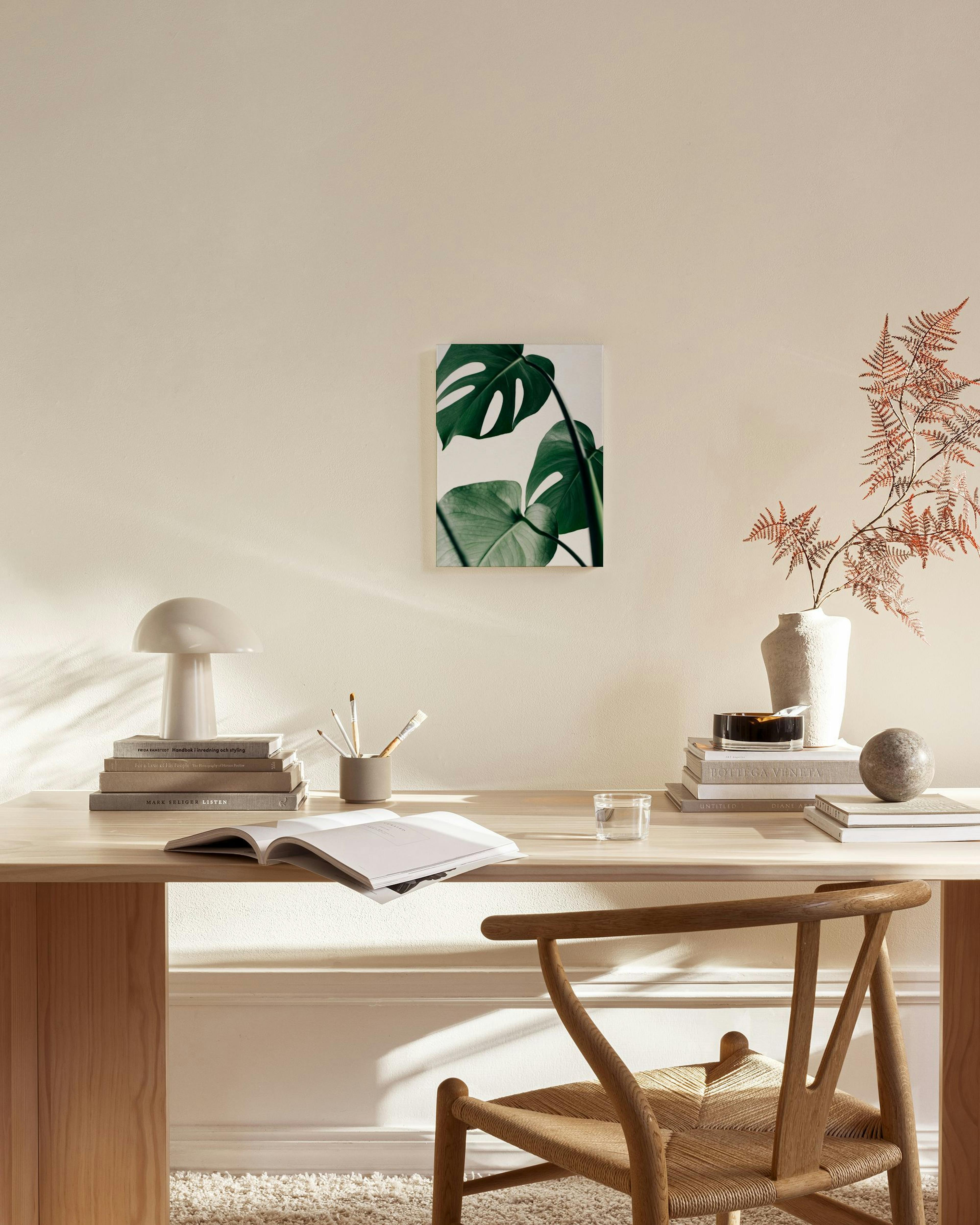 Toile Monstera verte accrochée dans un salon lumineux au-dessus dune commode en bois clair, avec chaise et table basse.