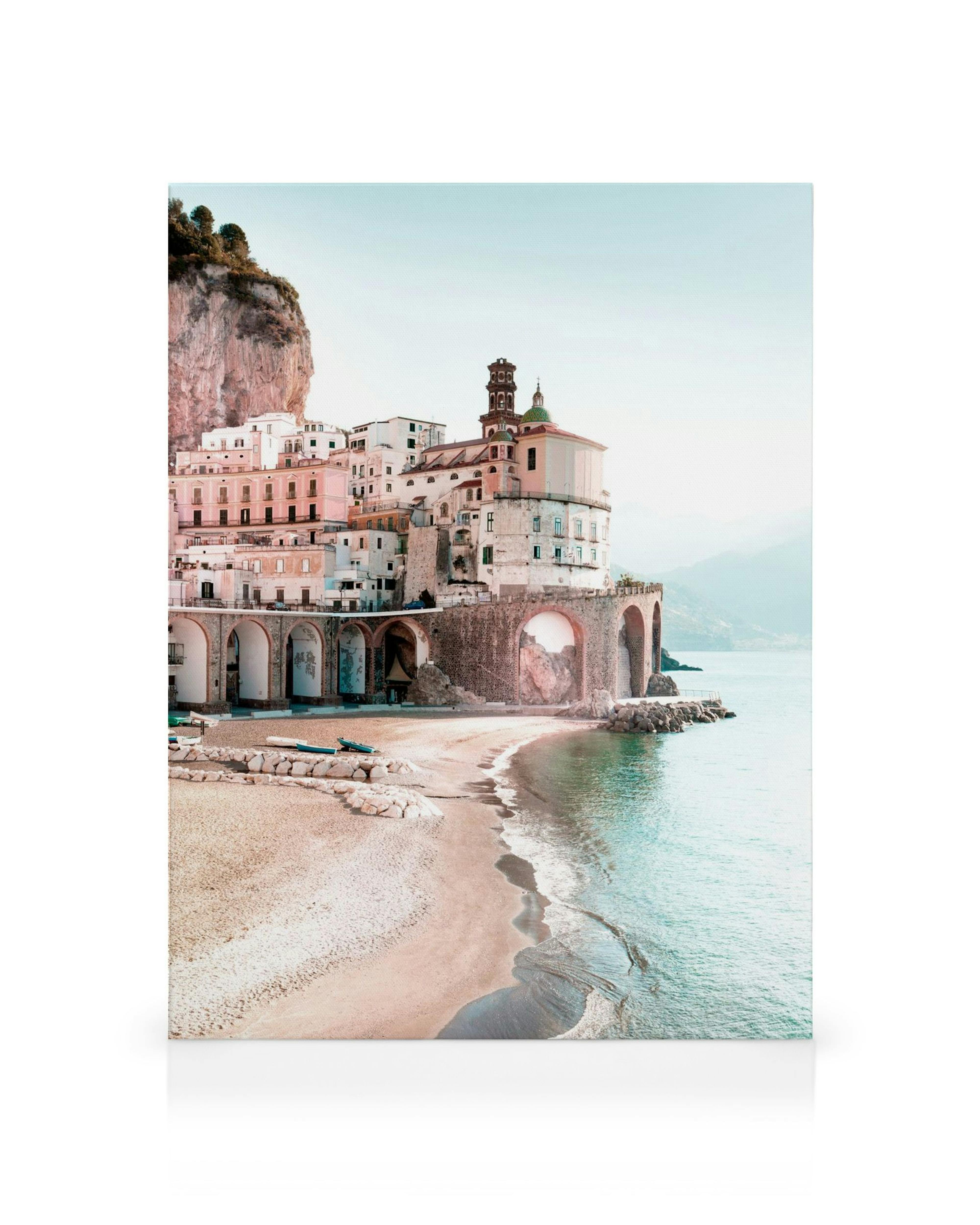Amalfi stadsgezicht canvas met roze, witte en bruine gebouwen, bogen en een zandstrand aan de kust onder een heldere lucht.