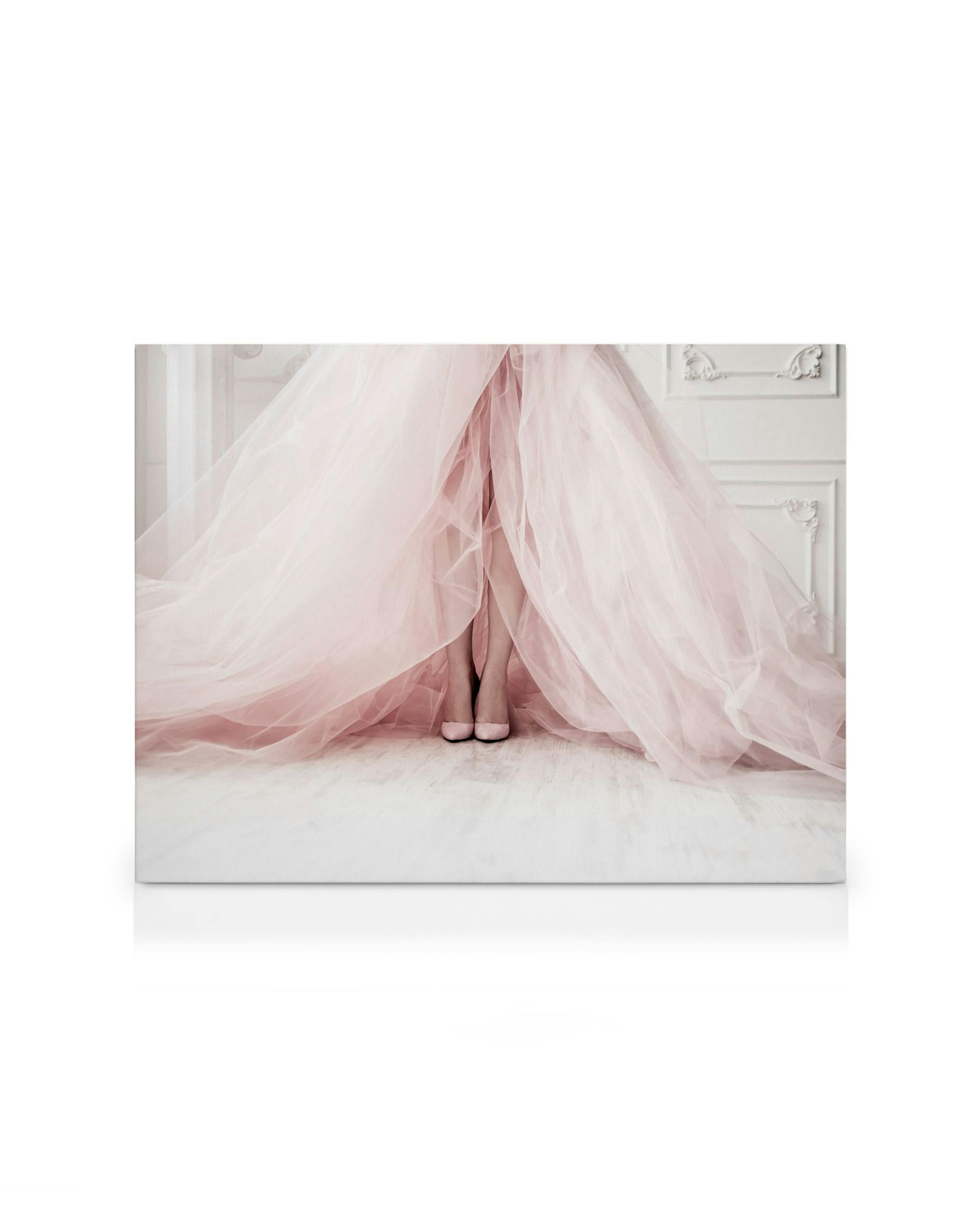 Fotografía de moda con tacones rosas bajo falda de tul flotante, contra fondo claro y gabinete blanco.