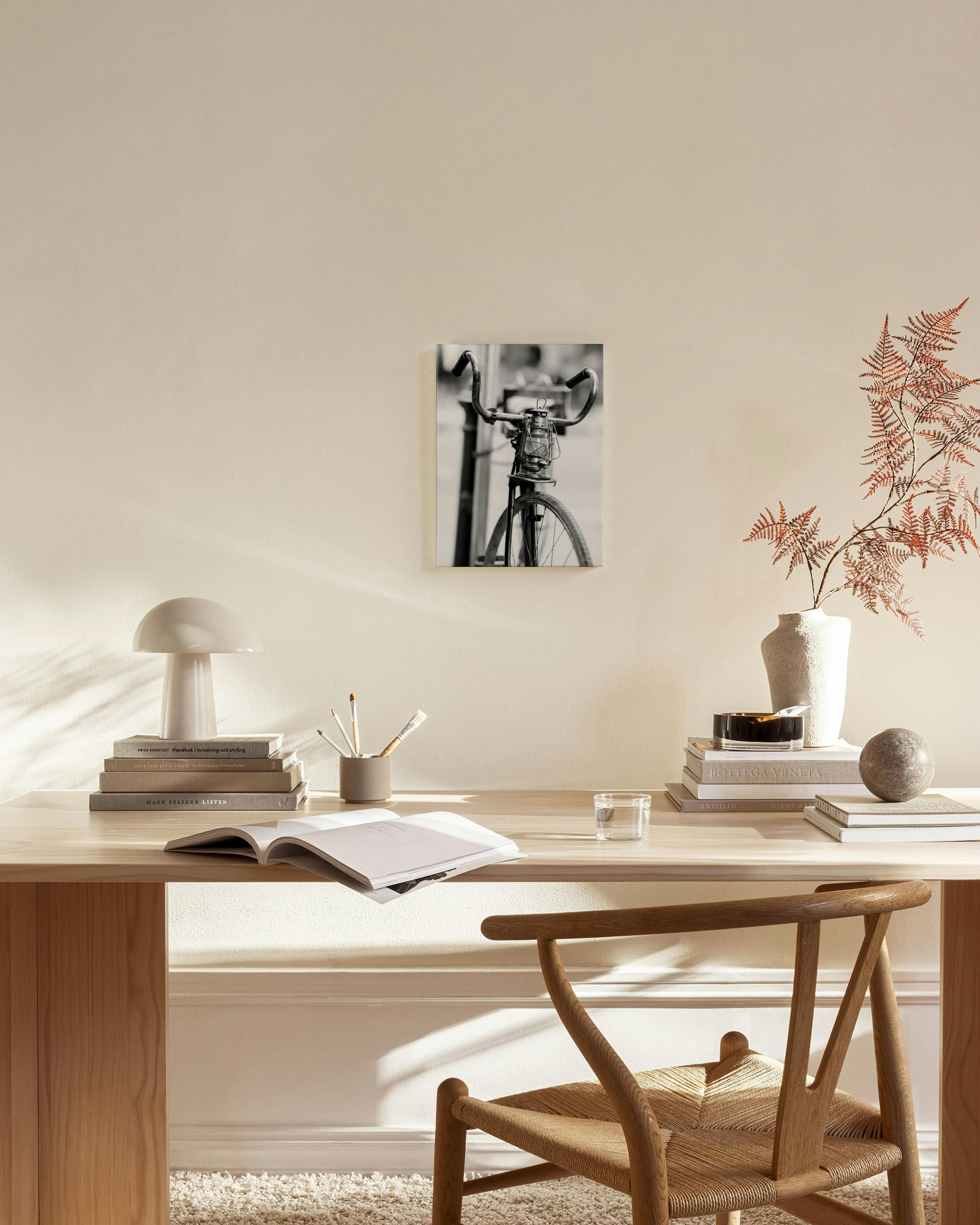 Zwart-wit canvas van een fiets met lamp, hangend boven een houten meubel in een lichte woonkamer.