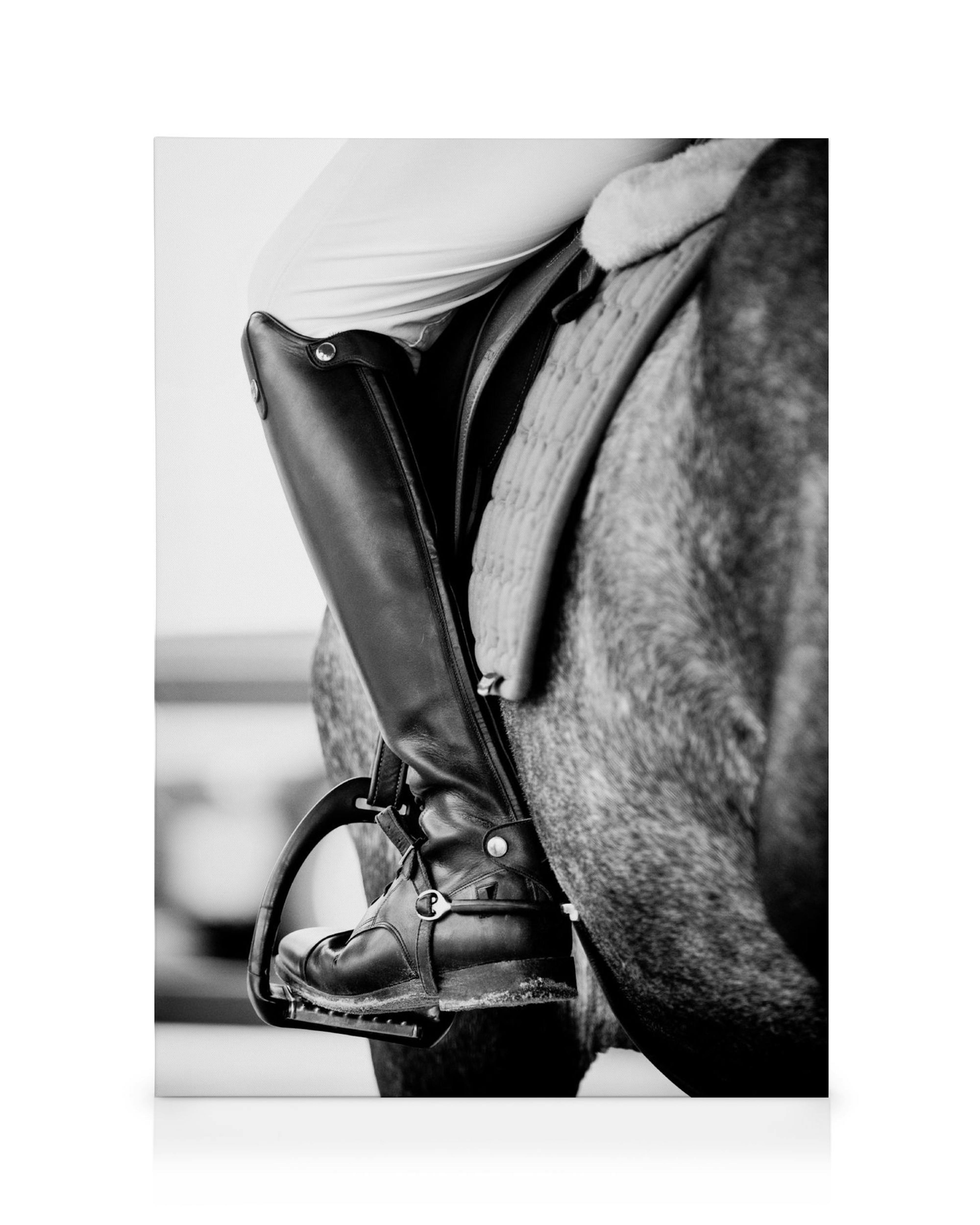 Black and white close-up of a riders black boot in a stirrup, on a saddled horse, equestrian sport art.