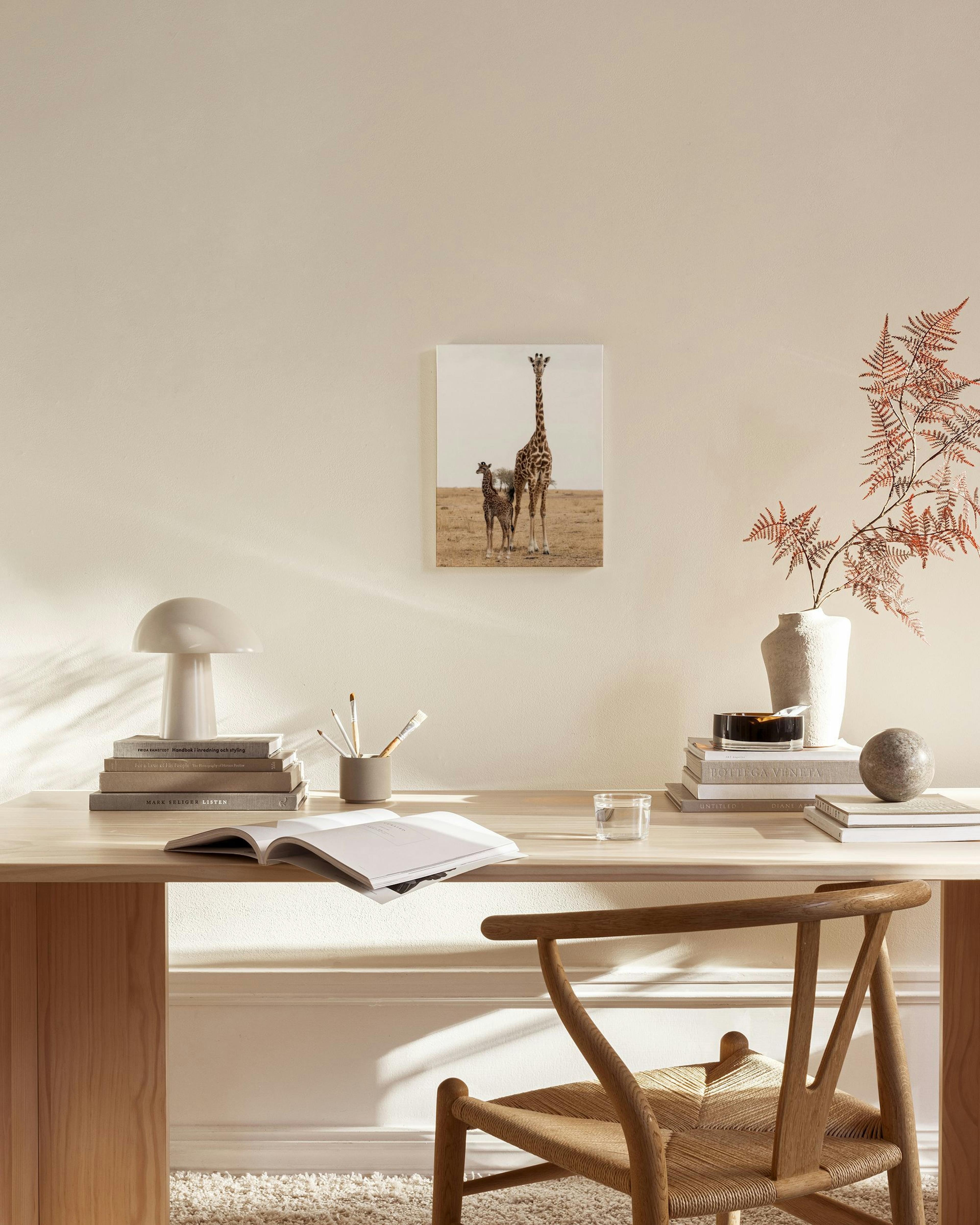 A canvas print of a mother giraffe and her calf in a dry landscape, displayed in a bright living room.