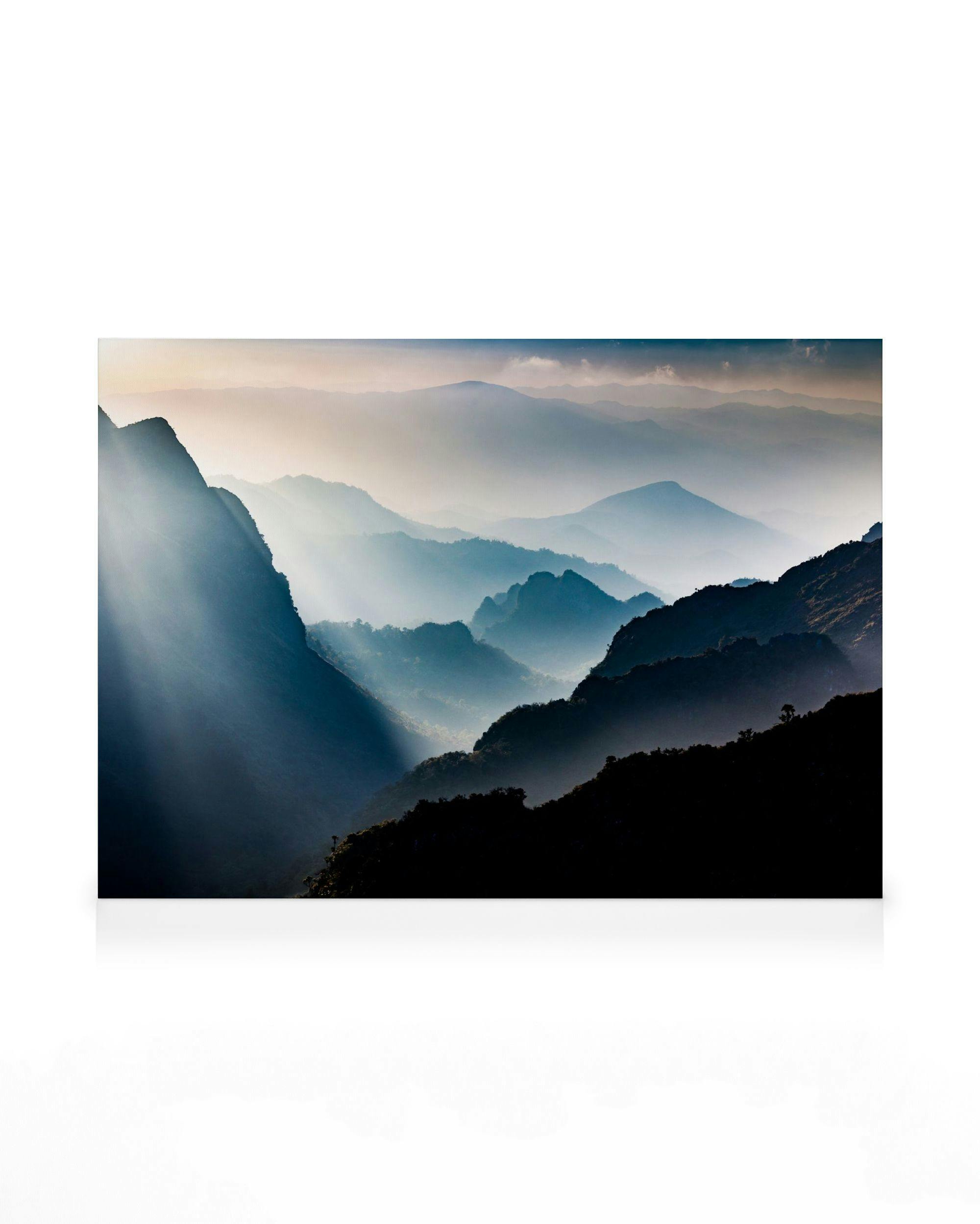 Foggy mountain landscape canvas with sun rays piercing through blue and white mist over dark peaks.