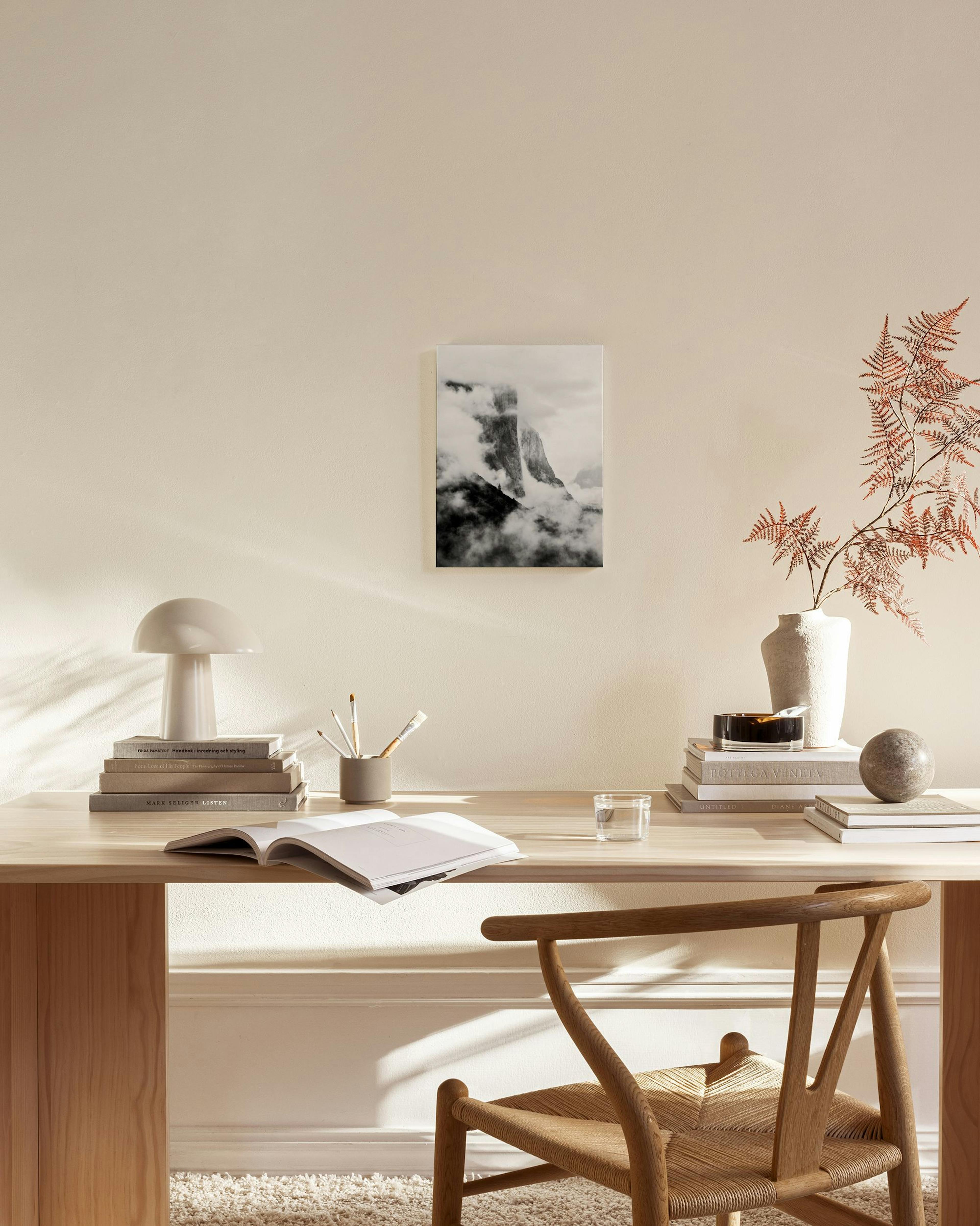 Zwart-wit canvas van een bergtop gehuld in mist, hangend boven een houten dressoir in een moderne woonkamer.