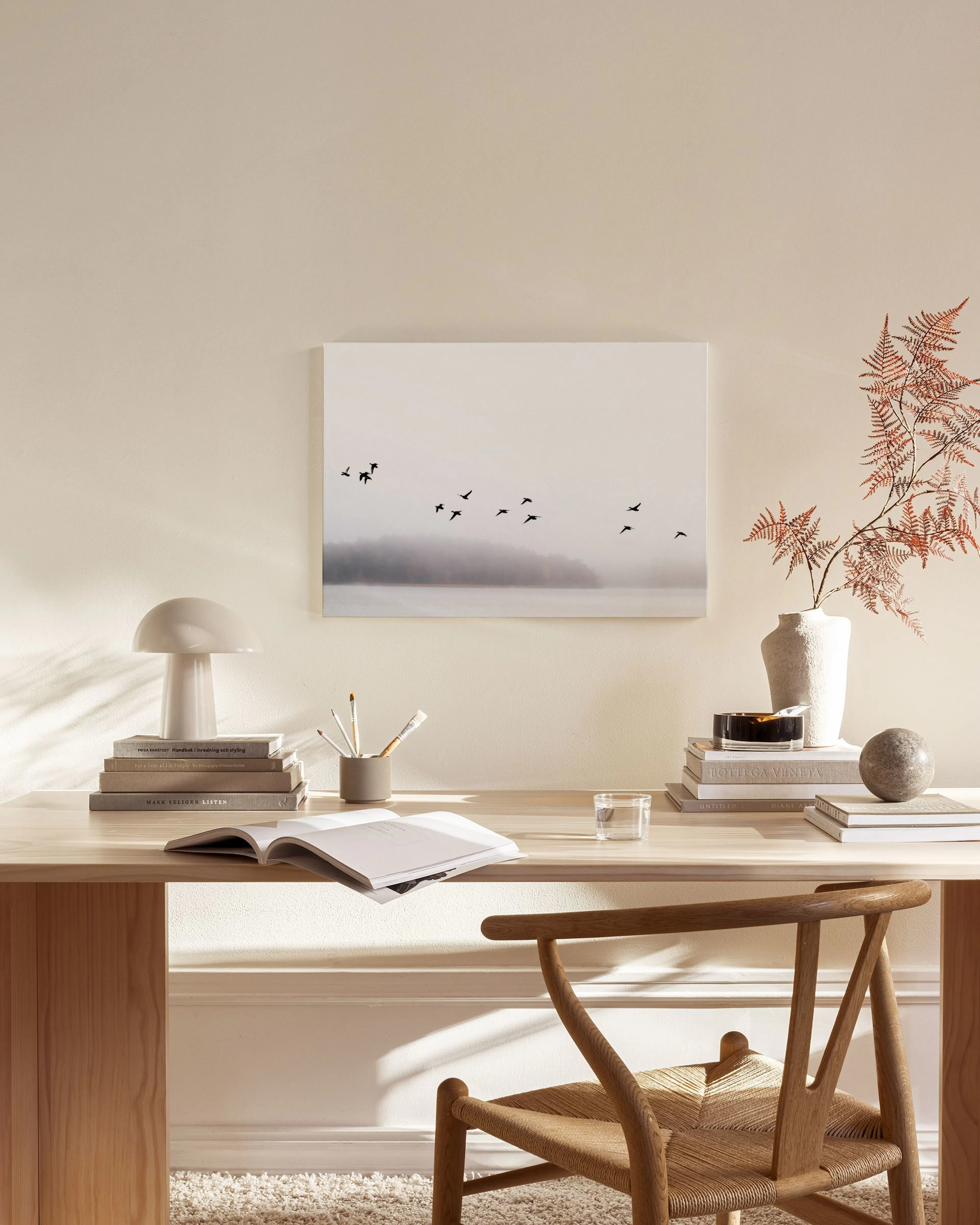 Monochromatic landscape canvas print of birds flying over a misty lake, hanging above a wooden console table in a minimalist liv