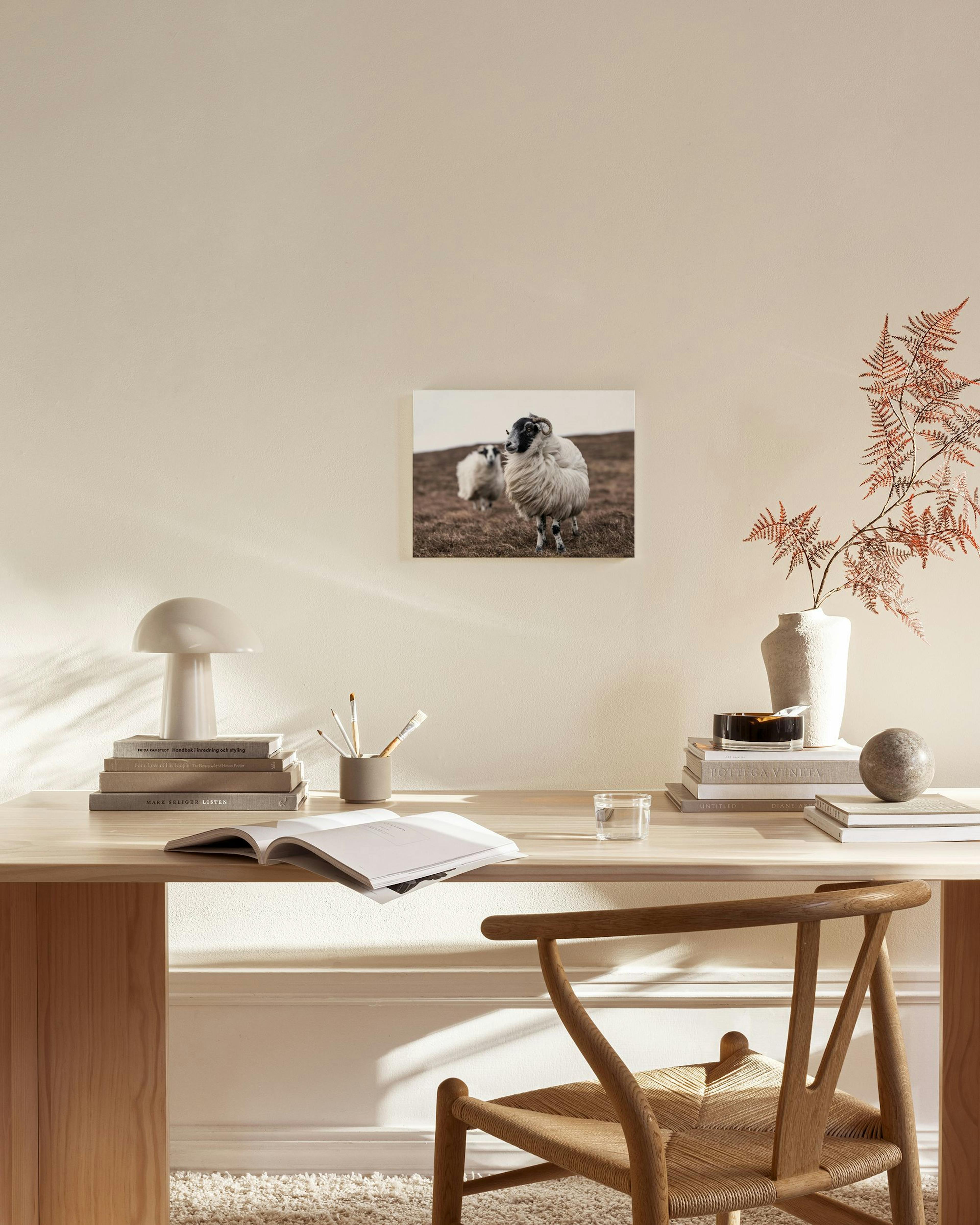 Leinwandbild mit zwei Schafen auf trockenem Feld, über einem Sideboard in einem beigen Wohnzimmer.