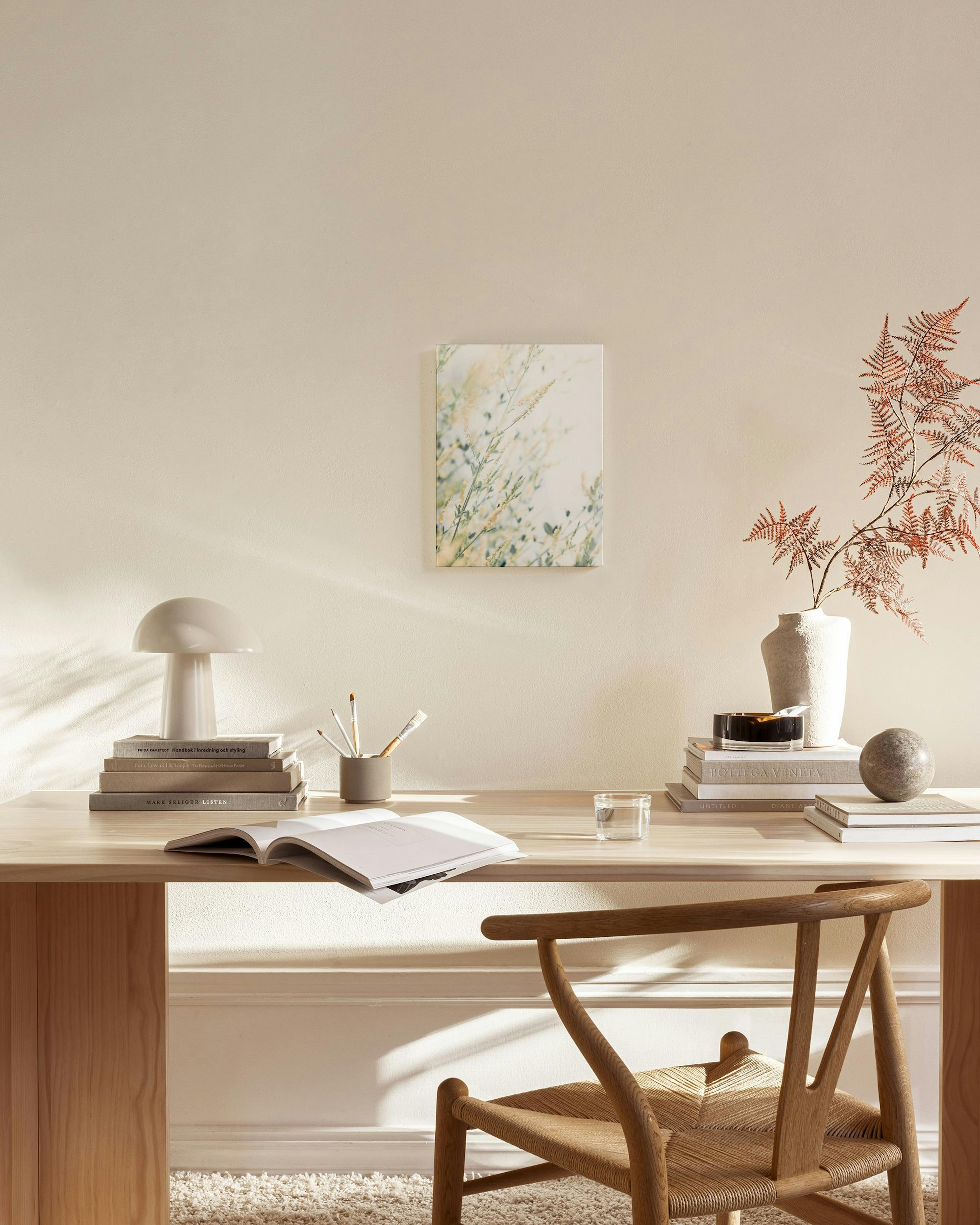 Toile de plantes floues aux tons vert pâle et beige, accrochée dans un salon moderne au-dessus dun banc en bois clair.