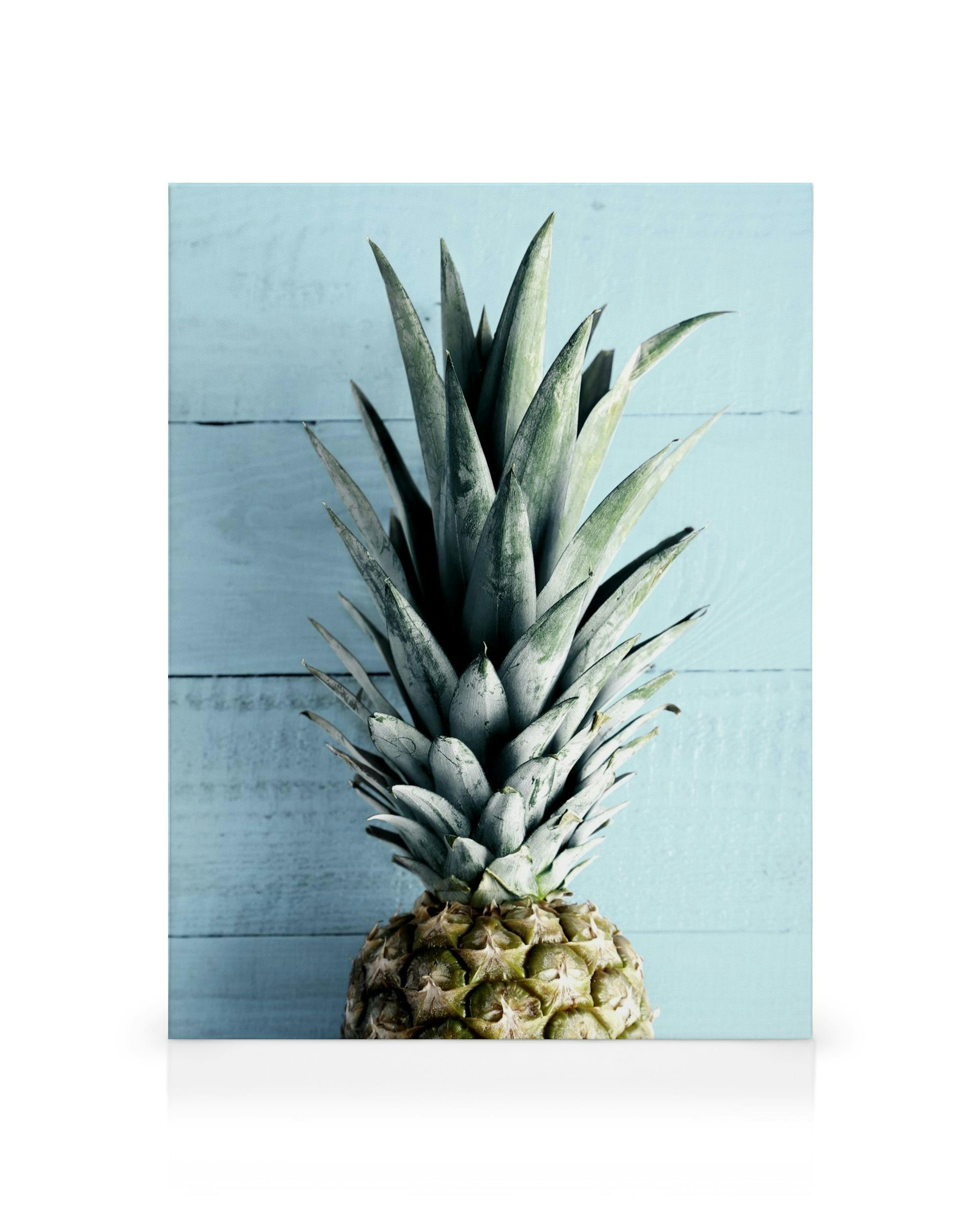 Levendige canvas print van een ananas met groene bladeren op een vervaagde blauwe houten achtergrond.
