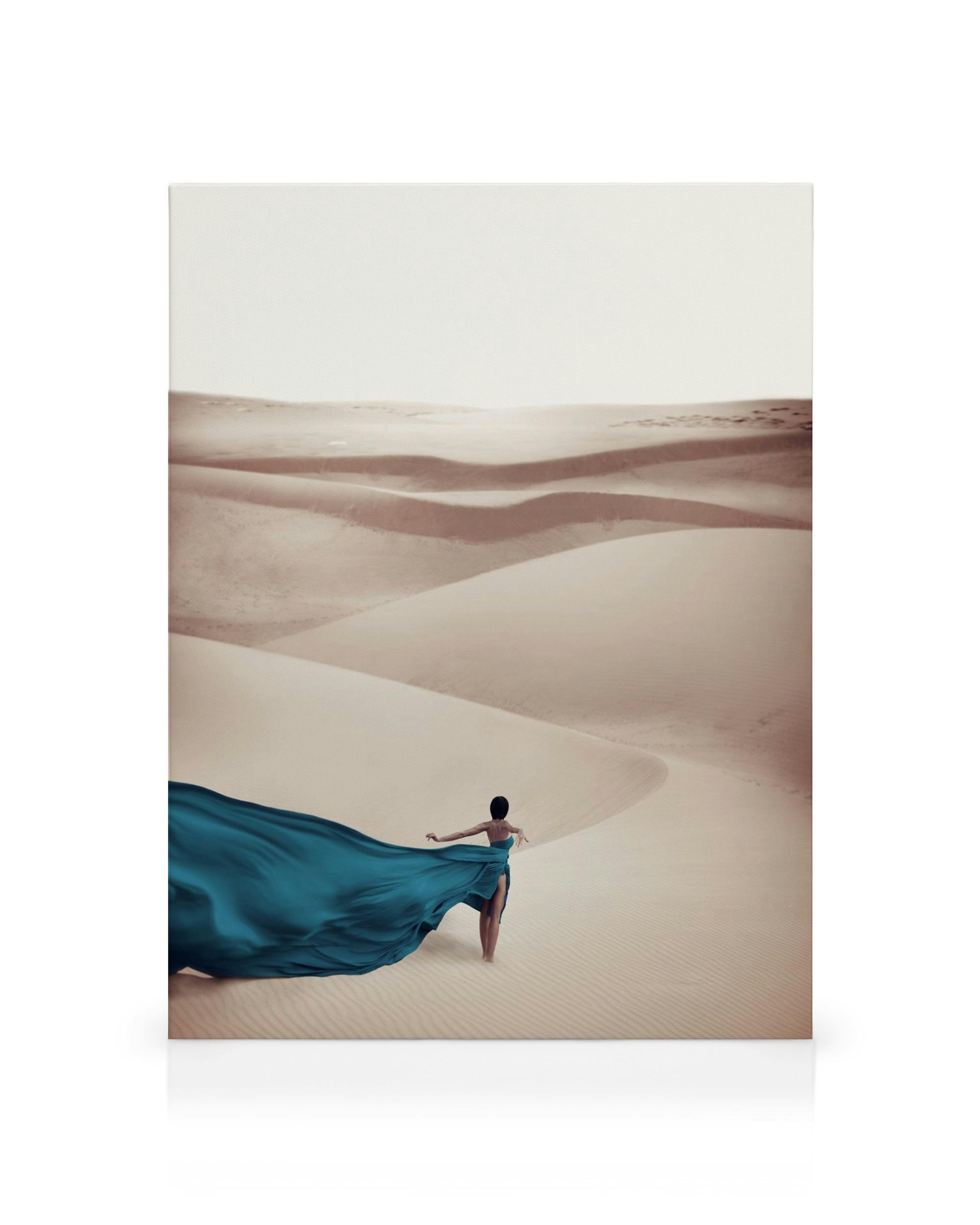 Vrouw met blauwe jurk in woestijn met zandduinen, vloeiende stof, elegantie