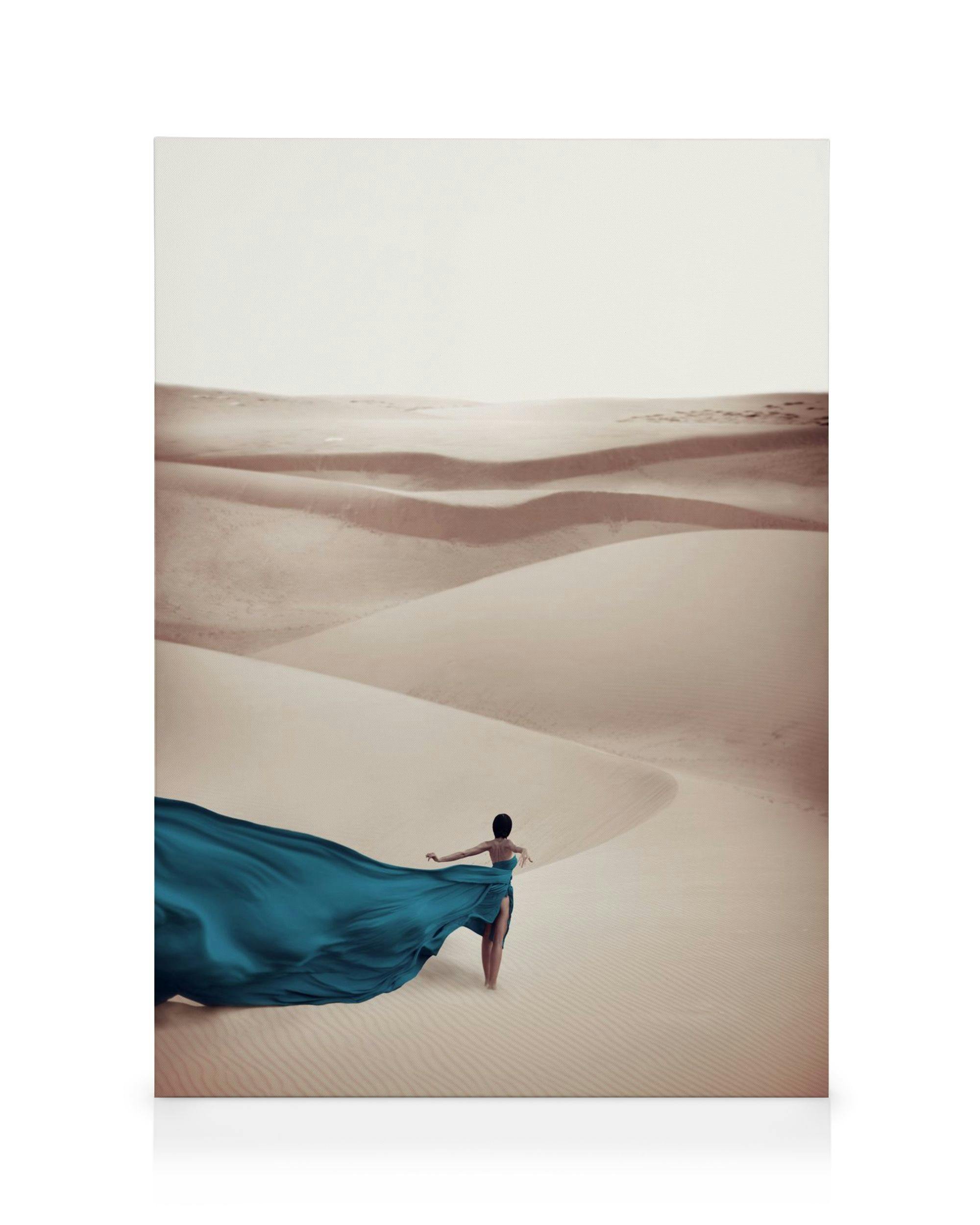 Woman in a flowing blue dress walking through a desert with sand dunes on a canvas print.