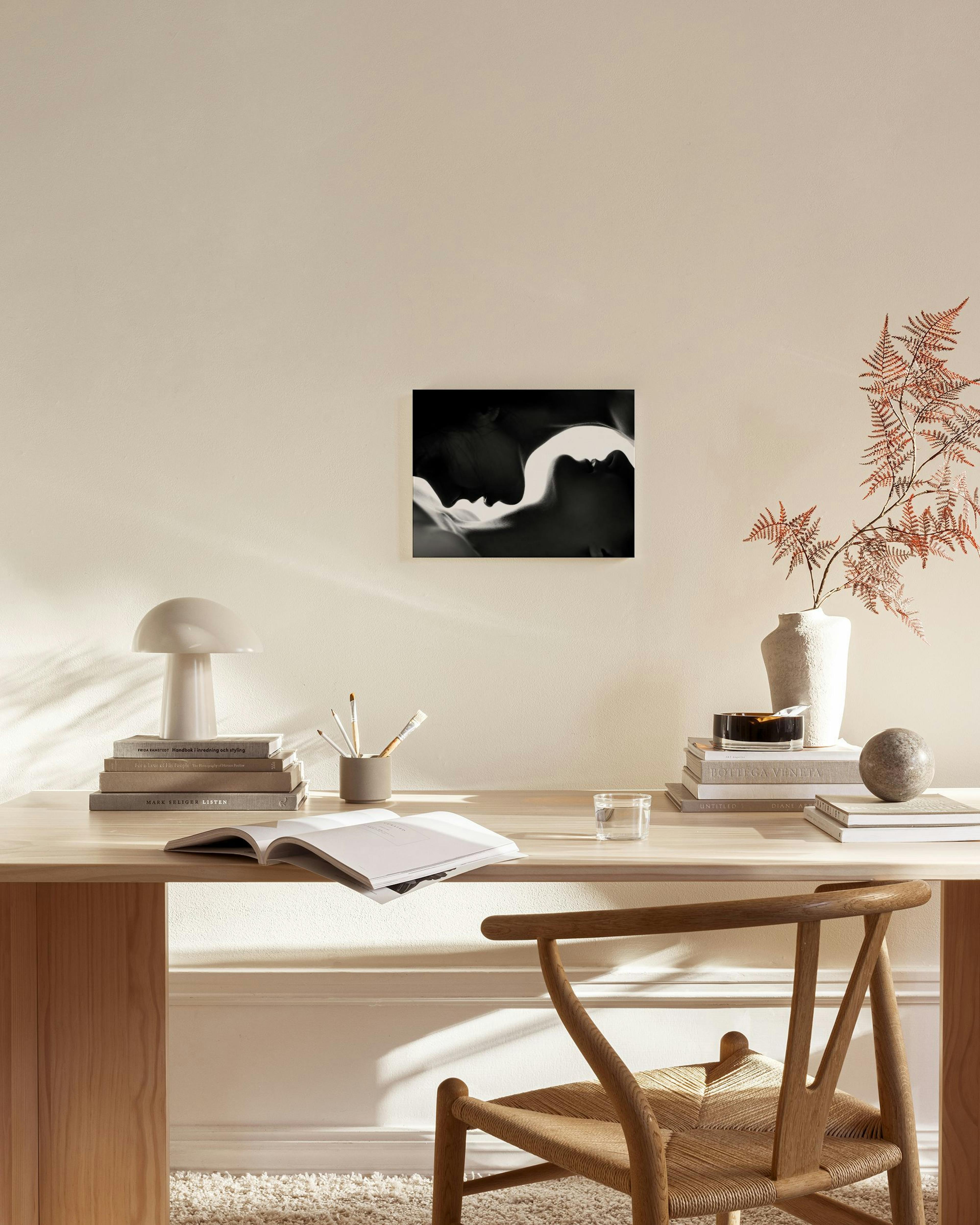 Leinwandbild mit zwei sich zugewandten Gesichtern in Schwarz-Weiß, hängend über einer Holzkommode mit Lampe und Büchern.