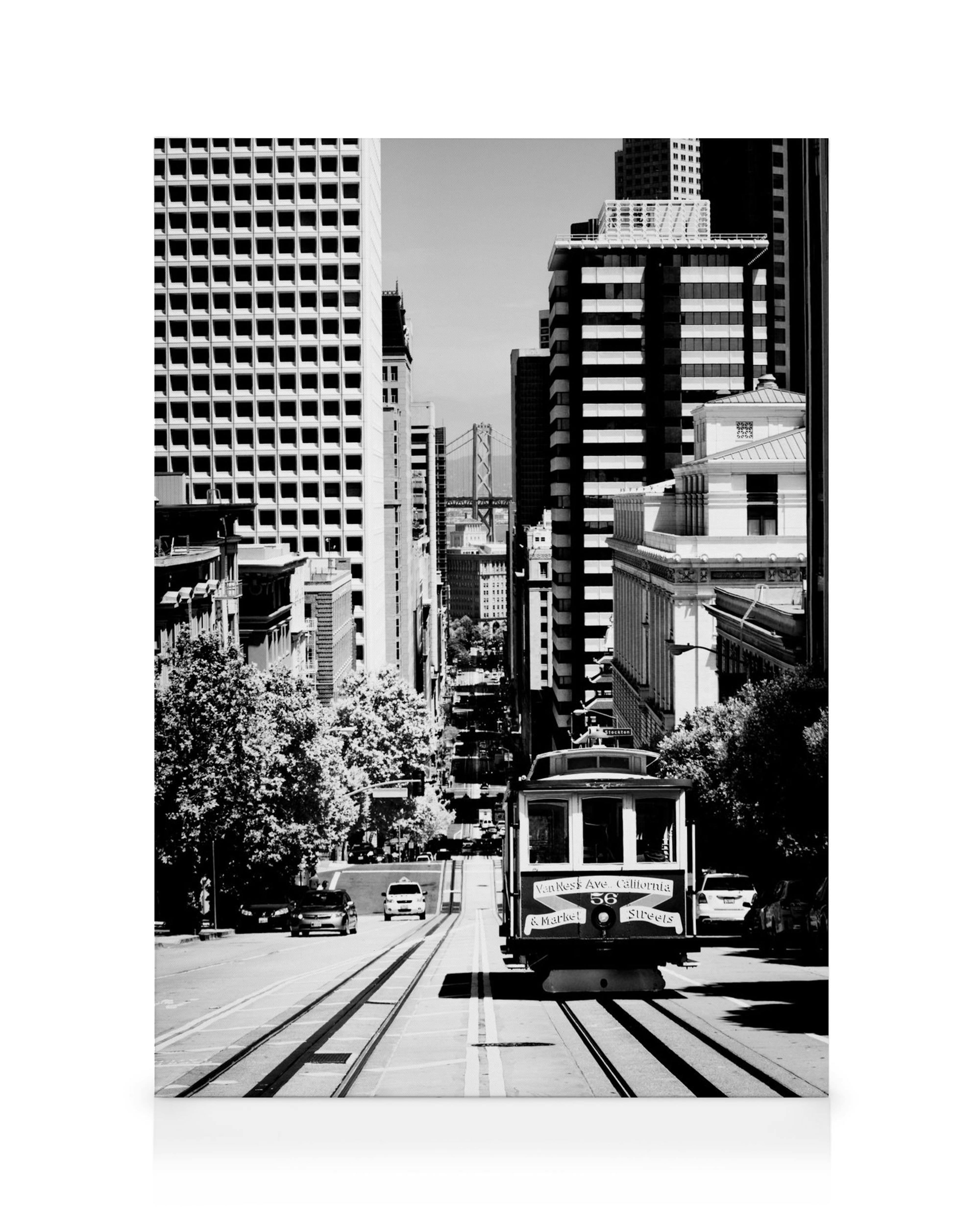 Černobílý obraz na plátně s lanovkou v San Franciscu na strmé ulici, s mostem v pozadí.