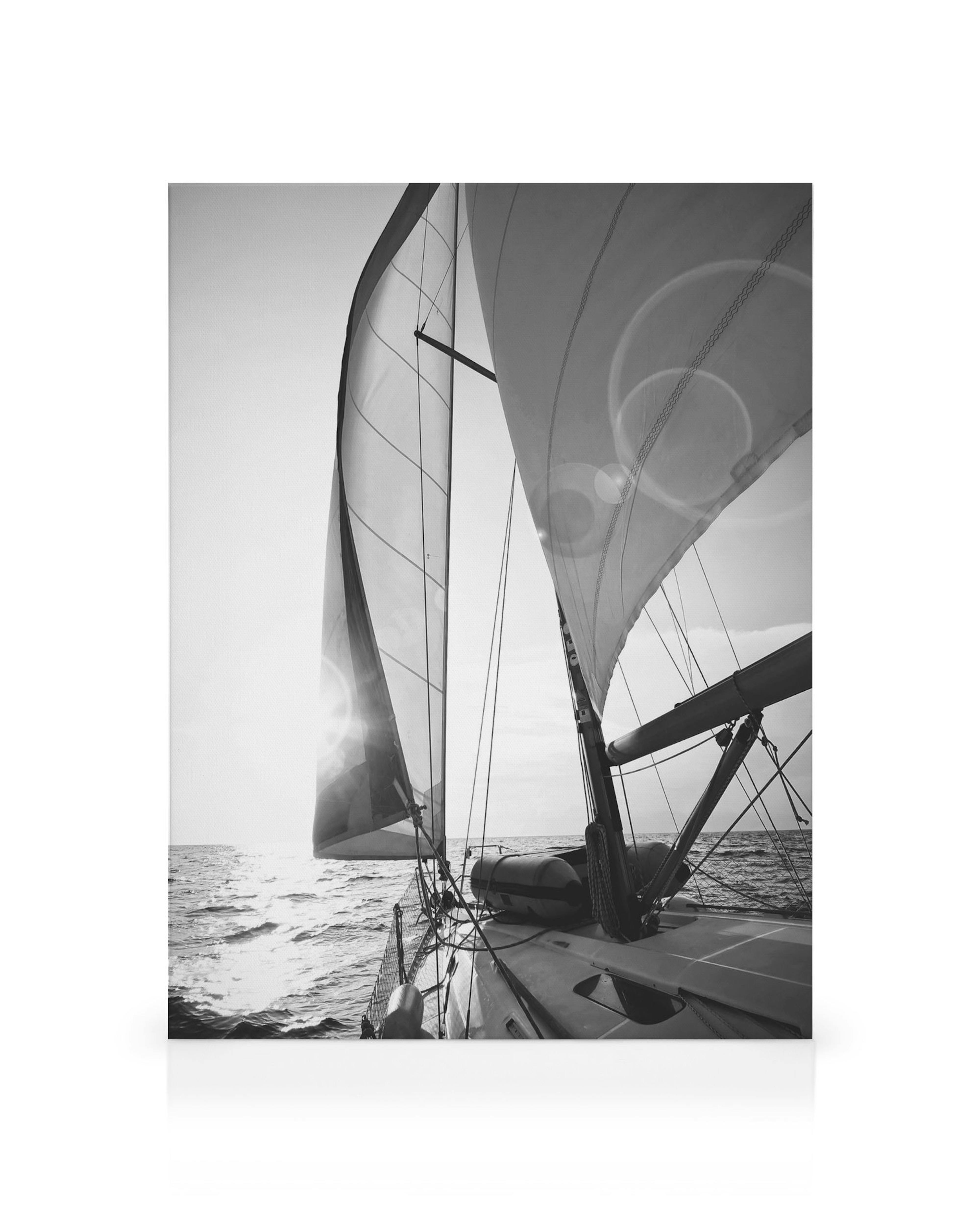 Schwarz-weißes Segelboot auf dem Meer mit vollen Segeln, Seilen und Sonnenlicht, das auf ruhigem Wasser glänzt.