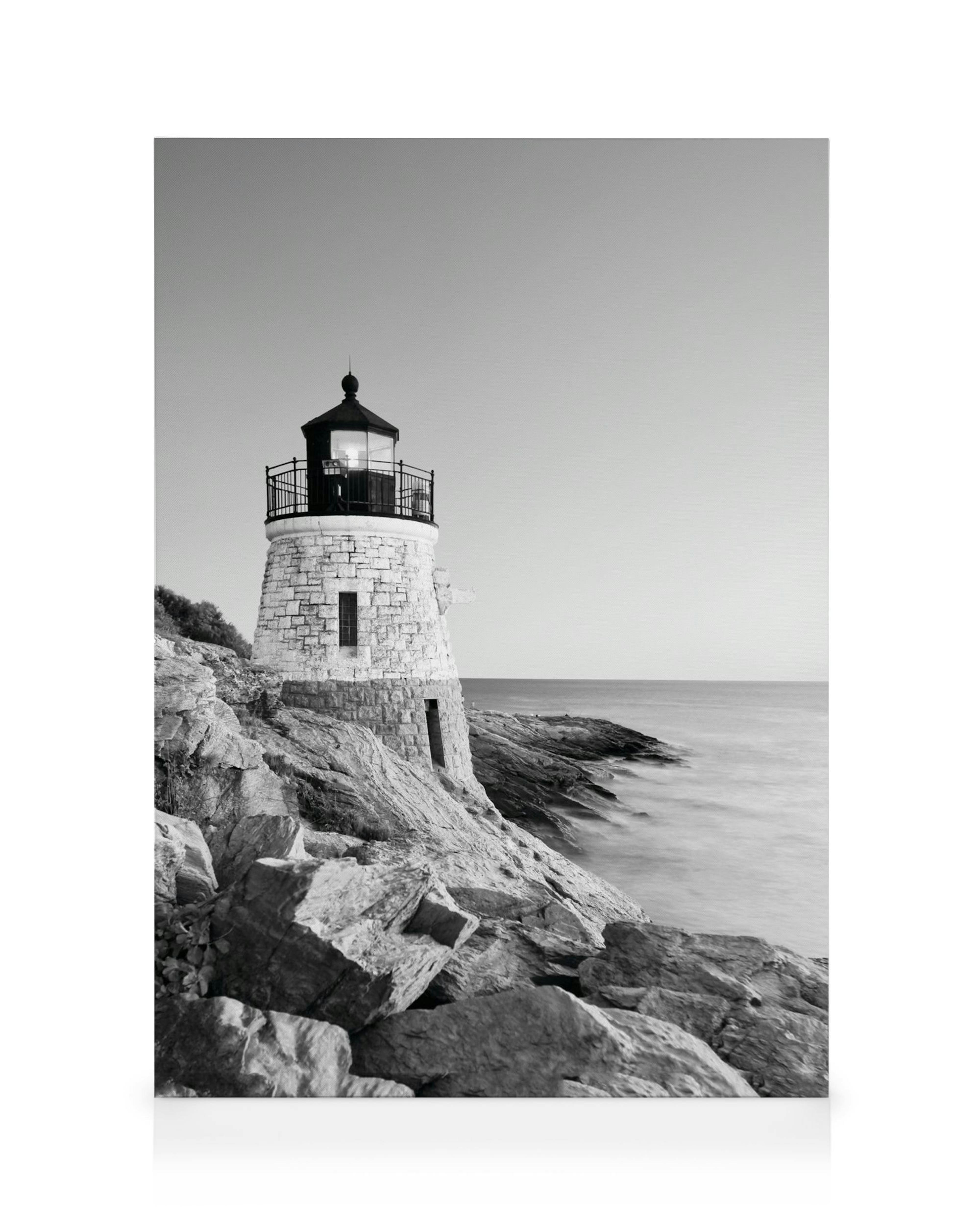 Black and white lighthouse on rocky shore with calm sea and clear sky, a serene coastal canvas print.