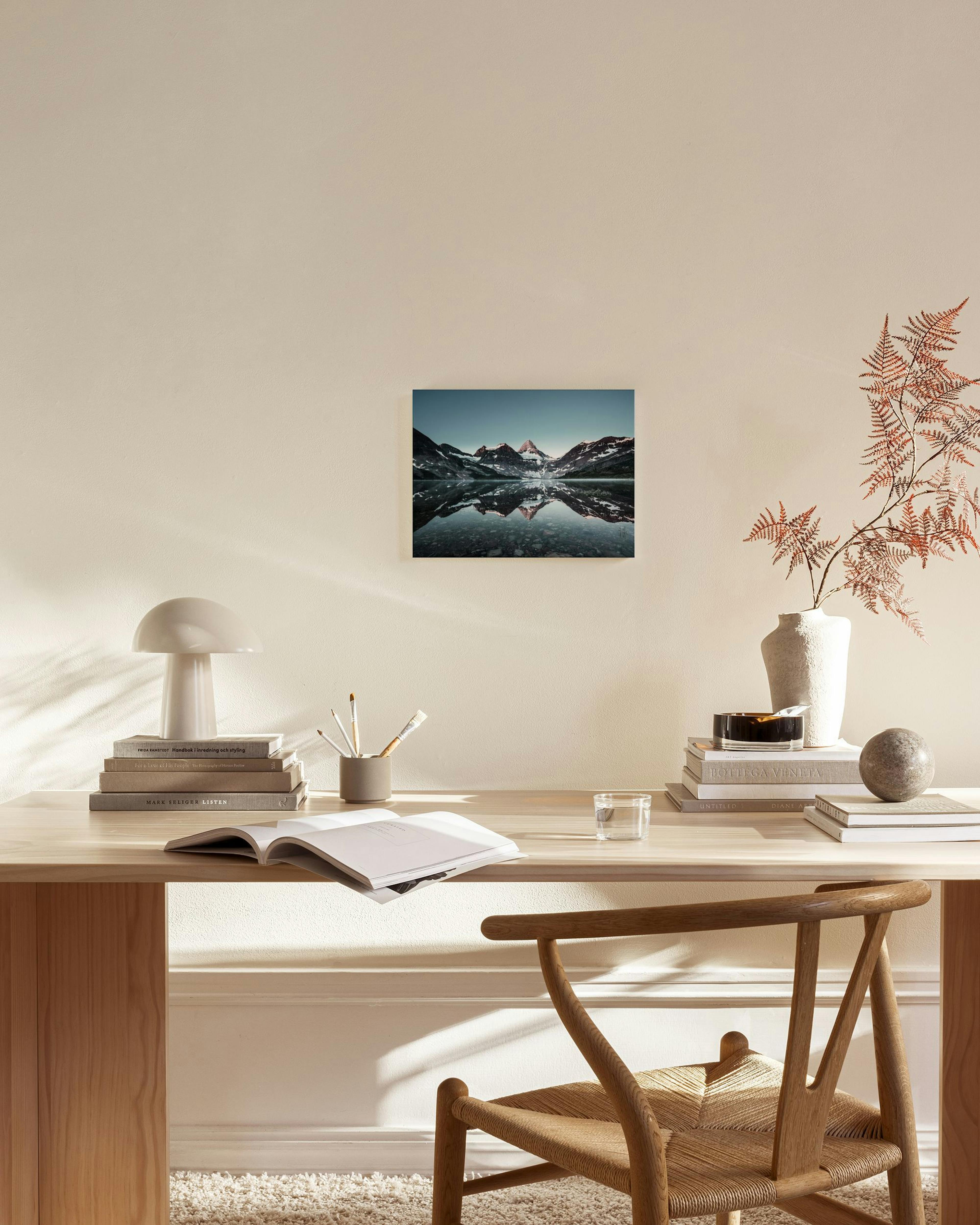 Canvas met een berglandschap weerspiegeld in een meer, hangend boven een houten dressoir in een moderne woonkamer.