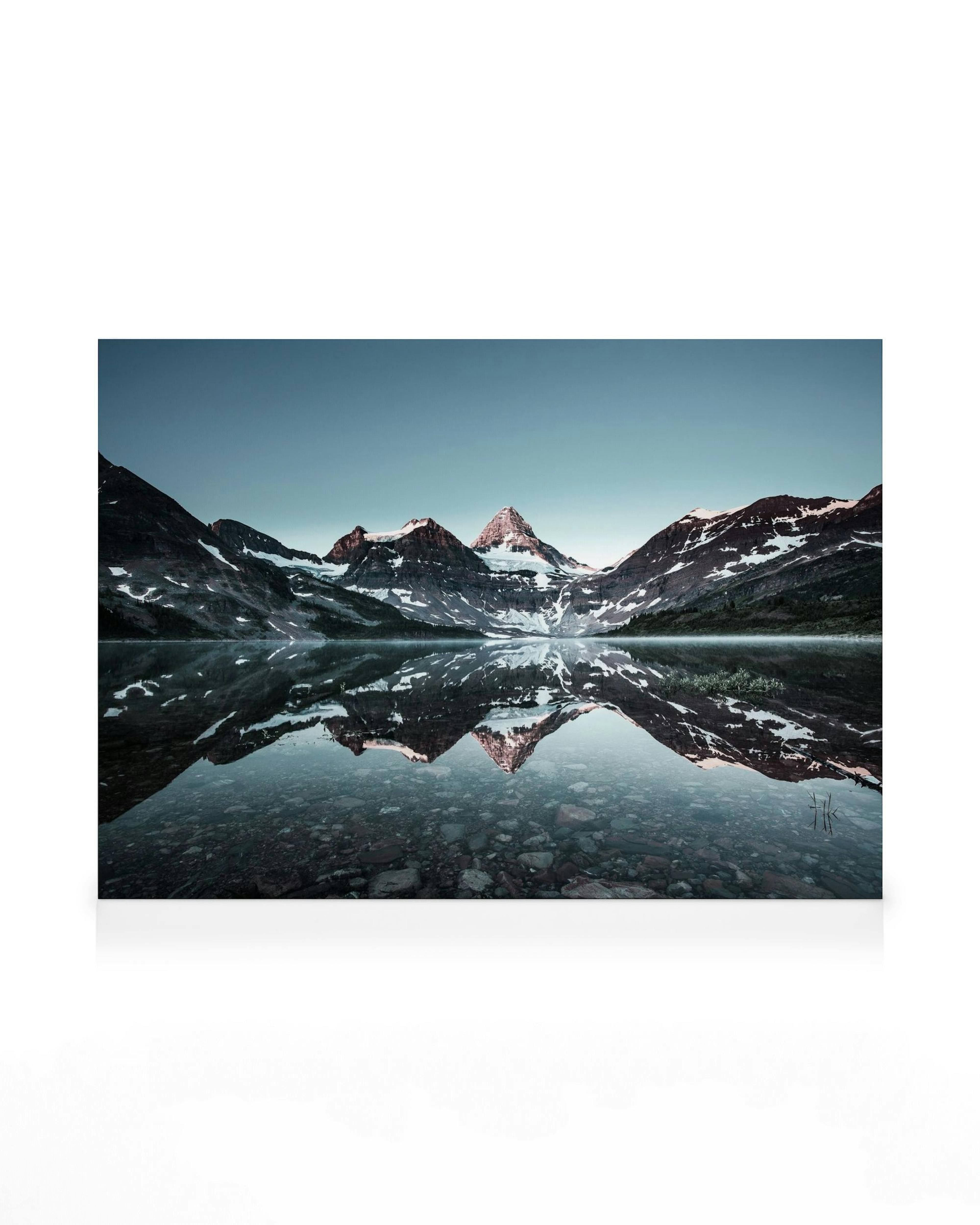 Canvas print of snow-capped mountains reflecting in a still lake under a clear blue sky, a calming nature scene.