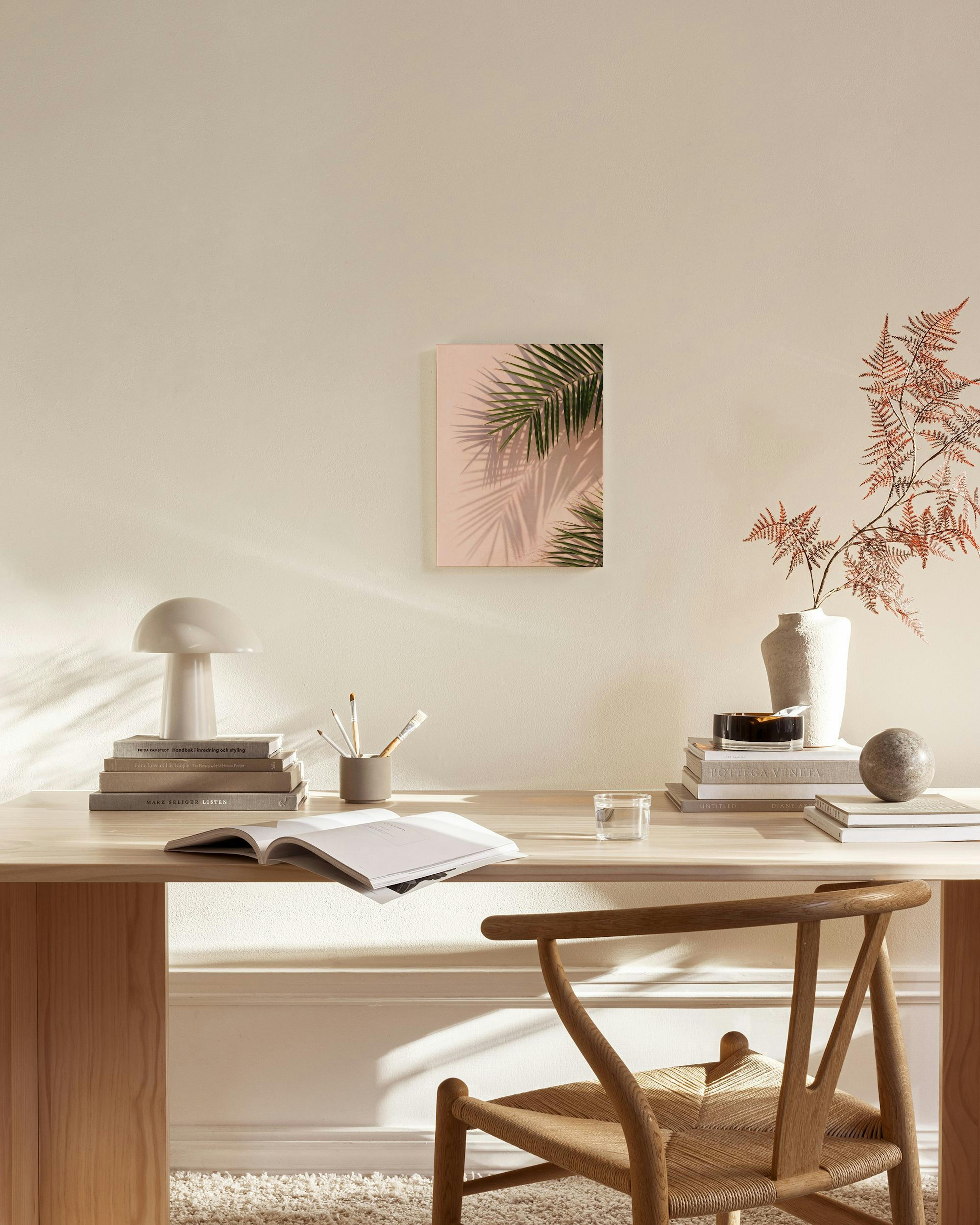 Toile de feuilles de palmier vertes et leurs ombres sur fond rose, accrochée au-dessus dun banc en bois dans un salon lumineux.