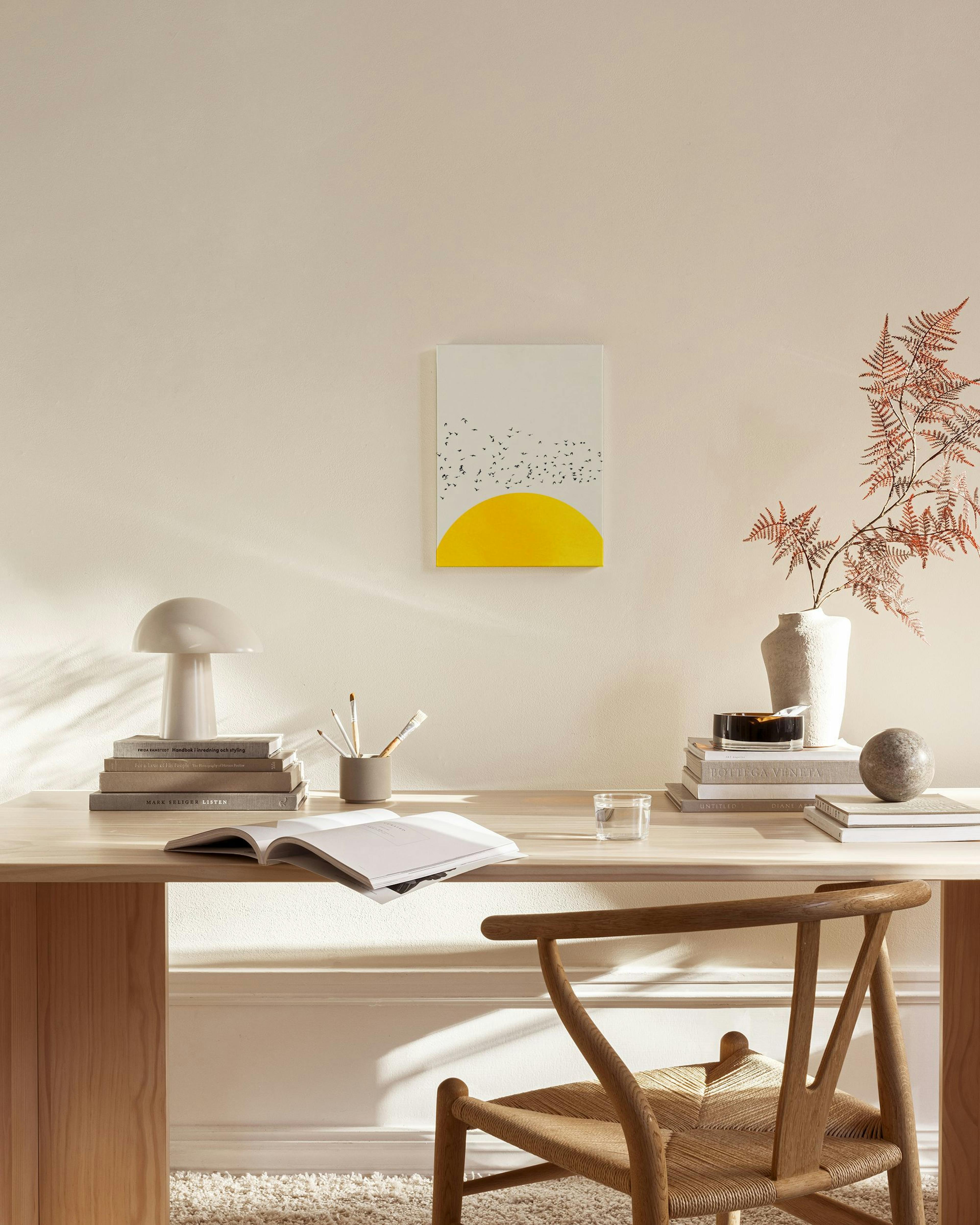 Toile murale avec un soleil jaune et des oiseaux noirs en vol, accrochée dans un salon lumineux au-dessus dun banc en bois.