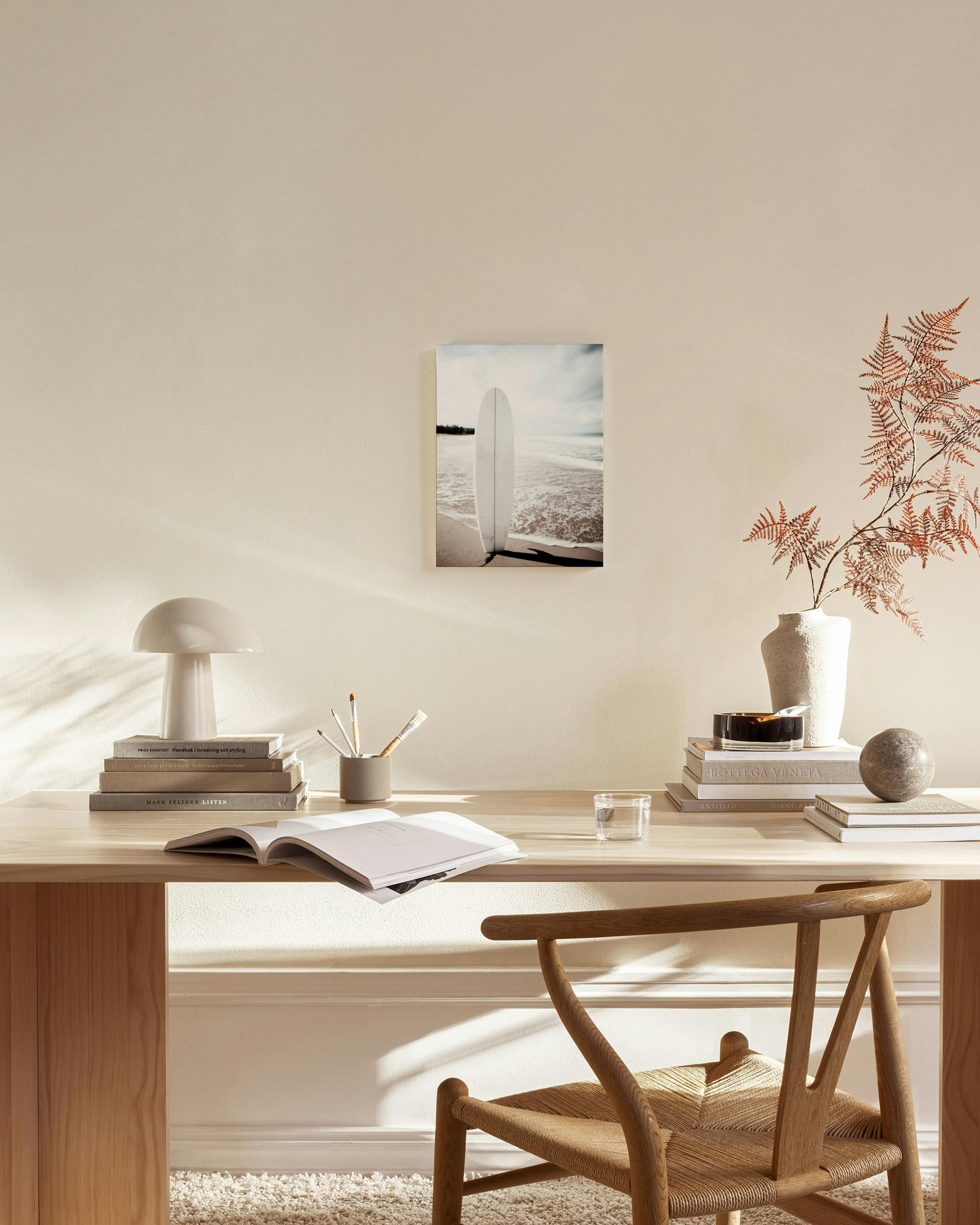 A surfboard propped on a sandy beach with ocean waves and a cloudy sky, displayed in a bright living room.