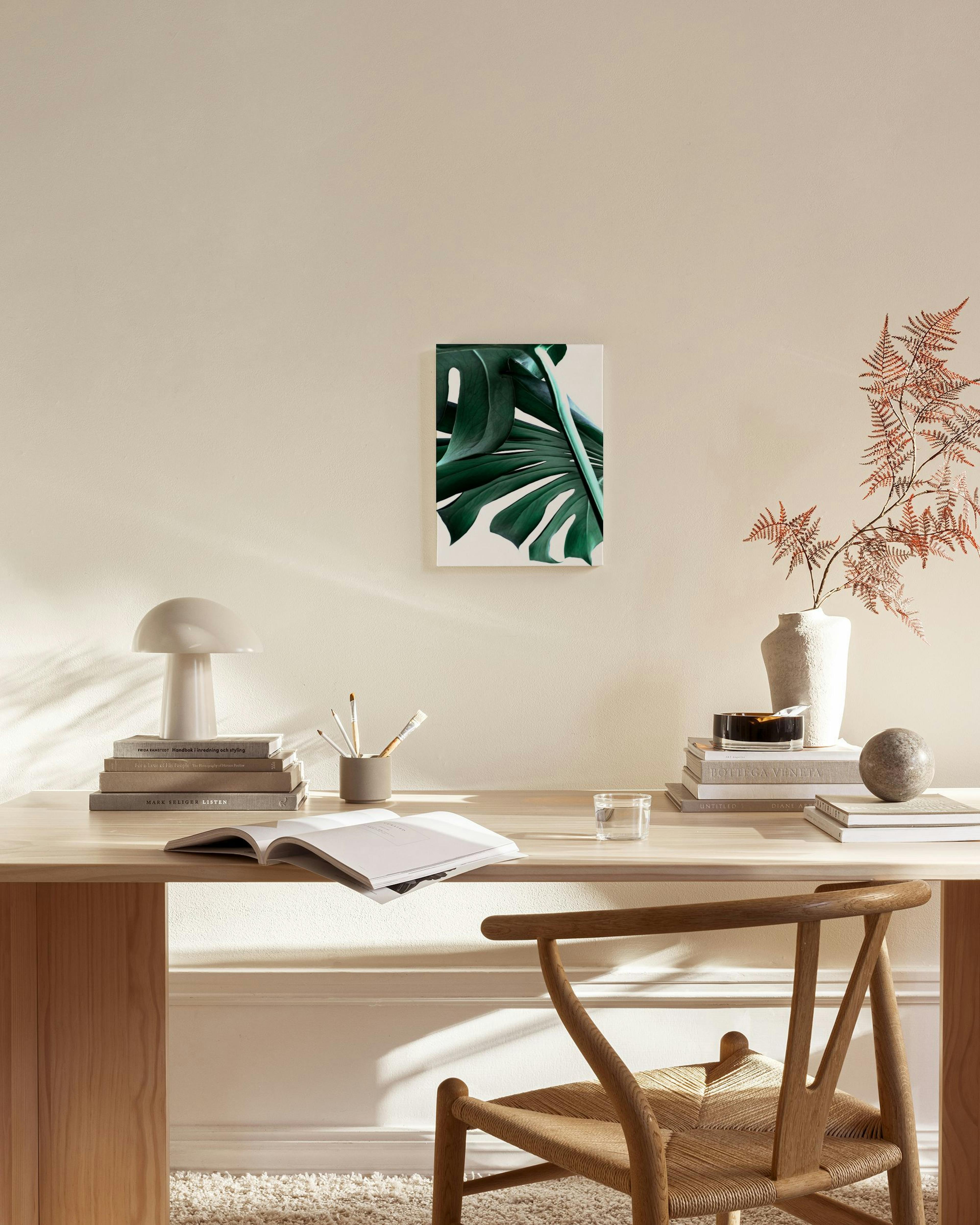 A canvas print of a large green monstera leaf on a white background, hanging in a minimalist living room.