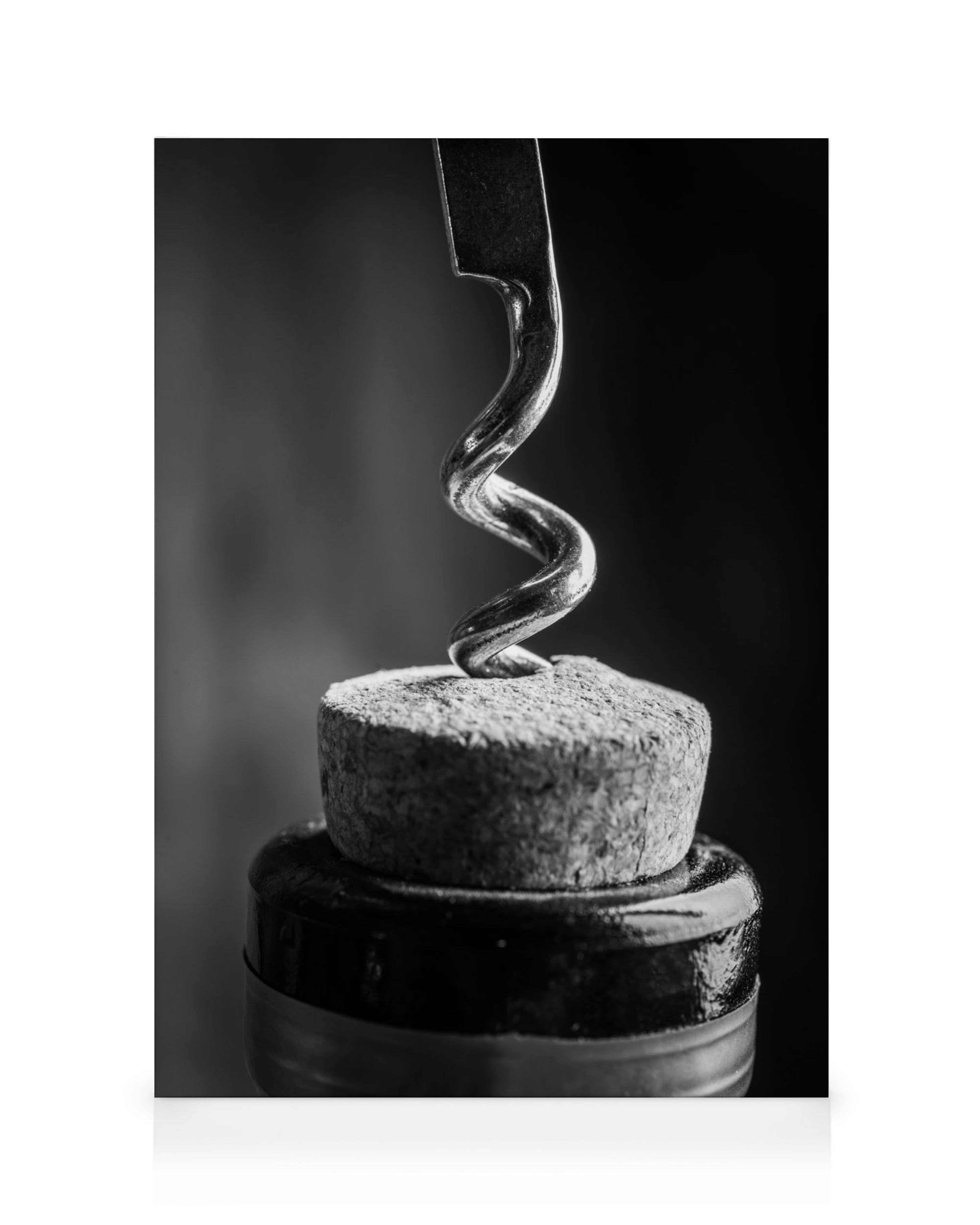 Sacacorchos metálico en espiral insertado en un corcho sobre una botella de vino, fotografía en blanco y negro.