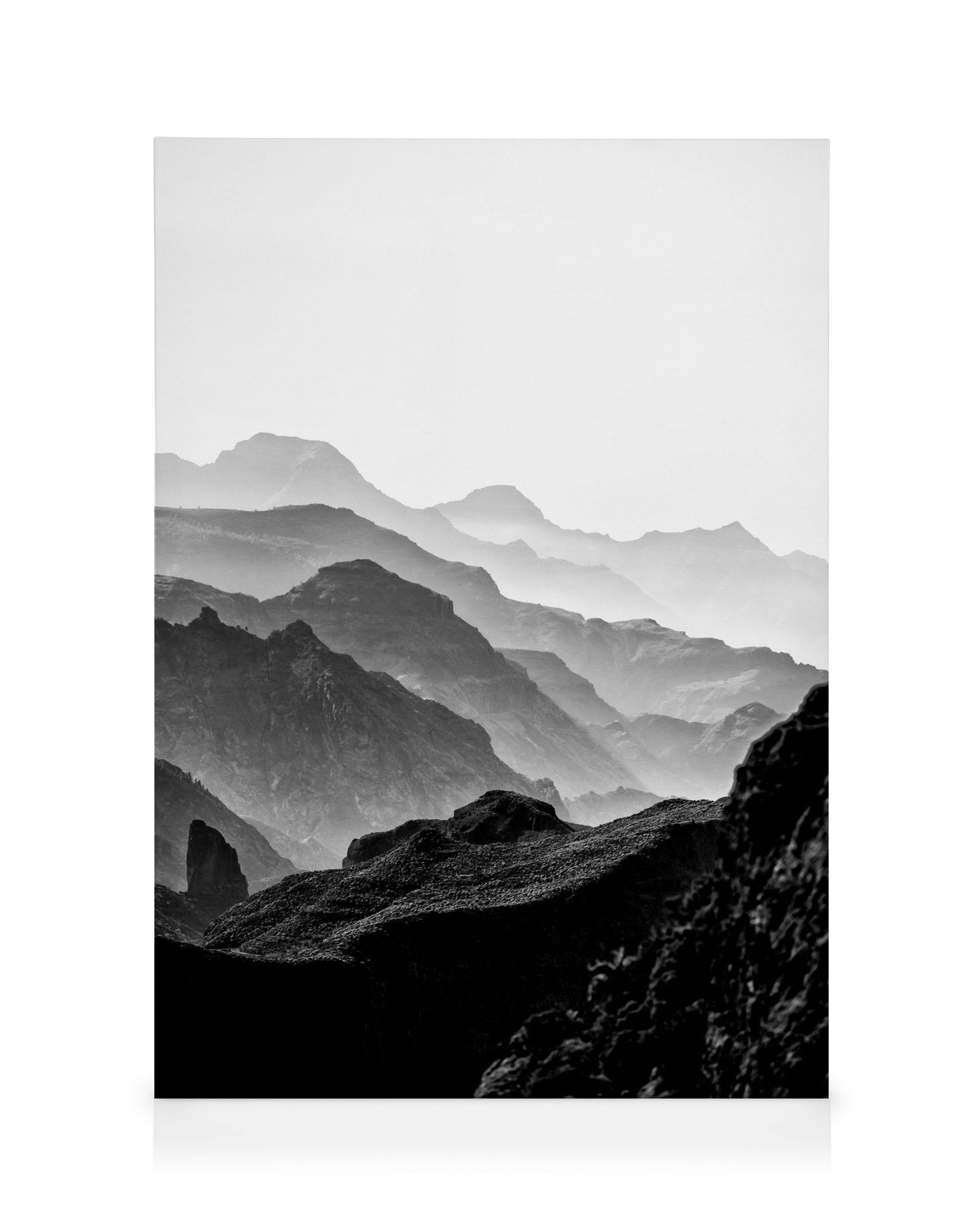 Black and white rocky mountain landscape with layered peaks fading into a misty sky, creating a dramatic, serene natural view.